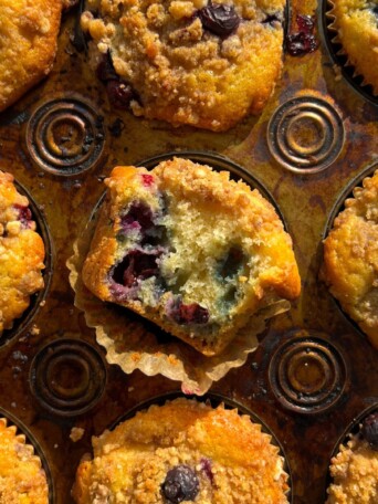 Blueberry Crumb Muffin with a bite taken out of it in the muffin pan.