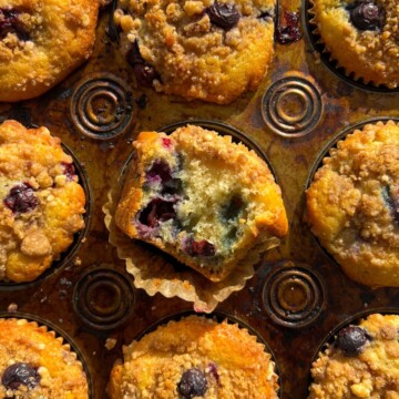 Blueberry Crumb Muffin with a bite taken out of it in the muffin pan.