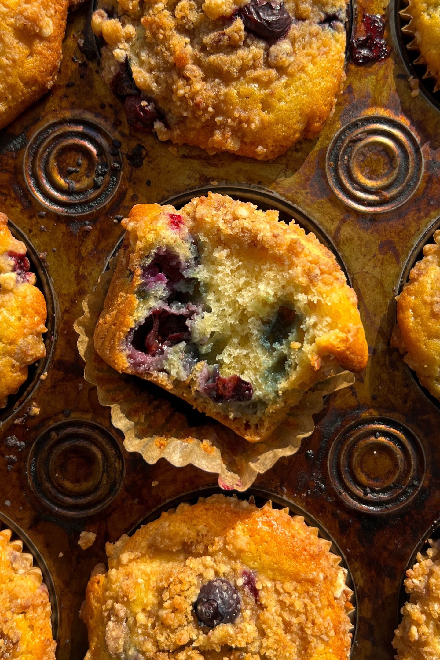 Blueberry Crumb Muffin with a bite taken out of it in the muffin pan.