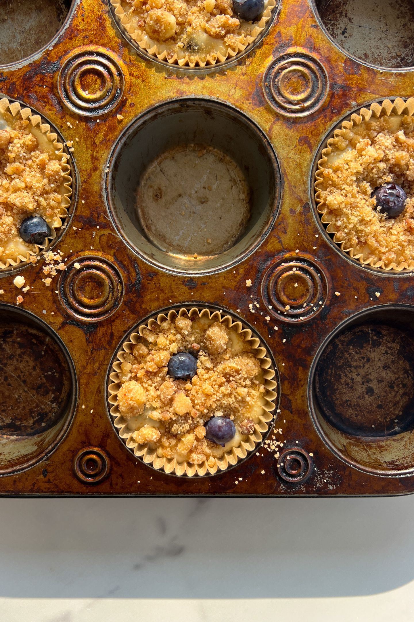 Batter in muffin liners topped with crumble and blueberries.