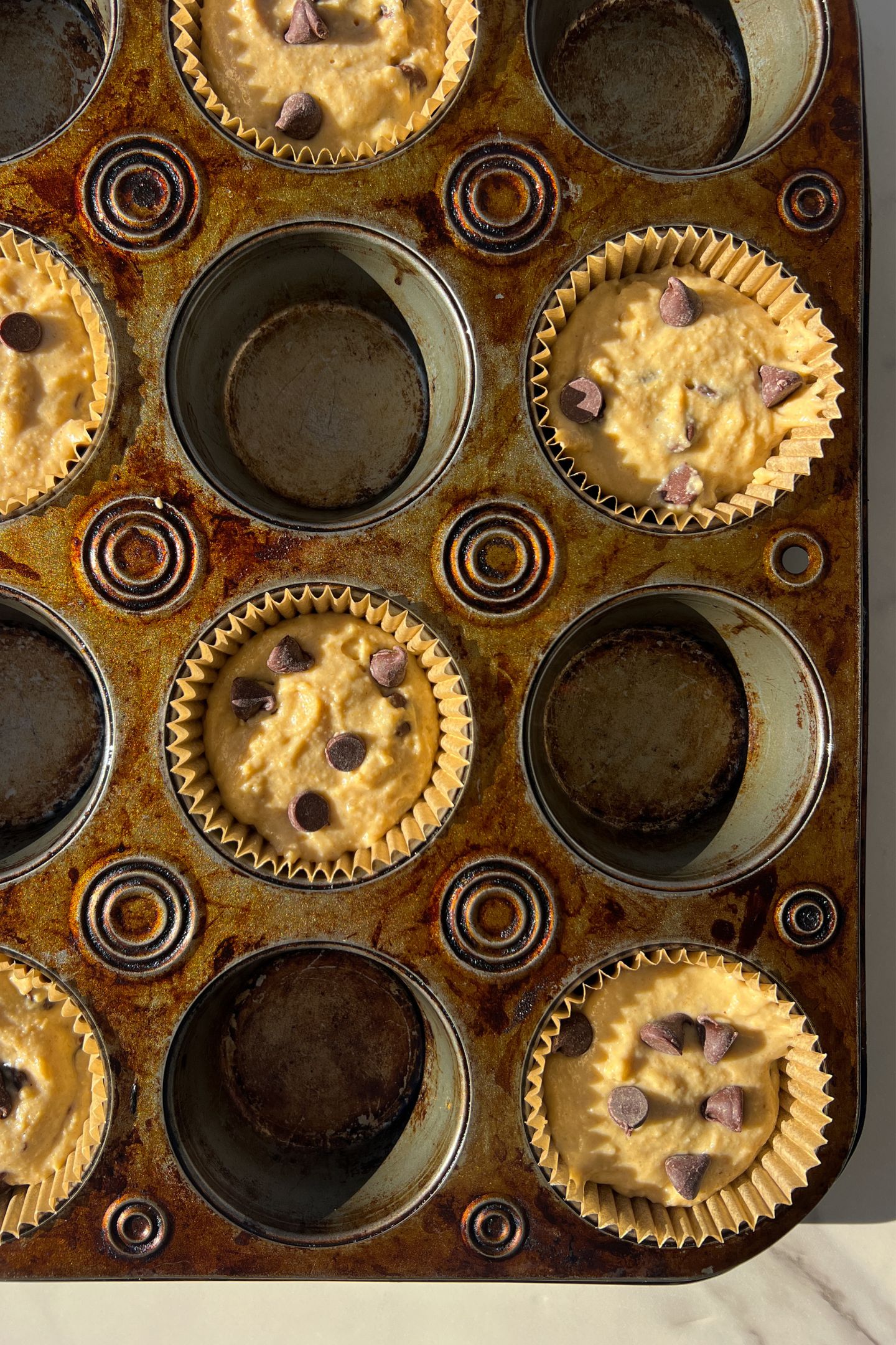 Muffin batter in muffin liners and topped with extra chocolate chips.