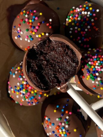 Chocolate cake pop with a bite taken out of it in a serving plate with more cake pops.