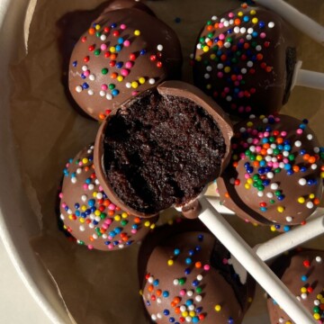 Chocolate cake pop with a bite taken out of it in a serving plate with more cake pops.