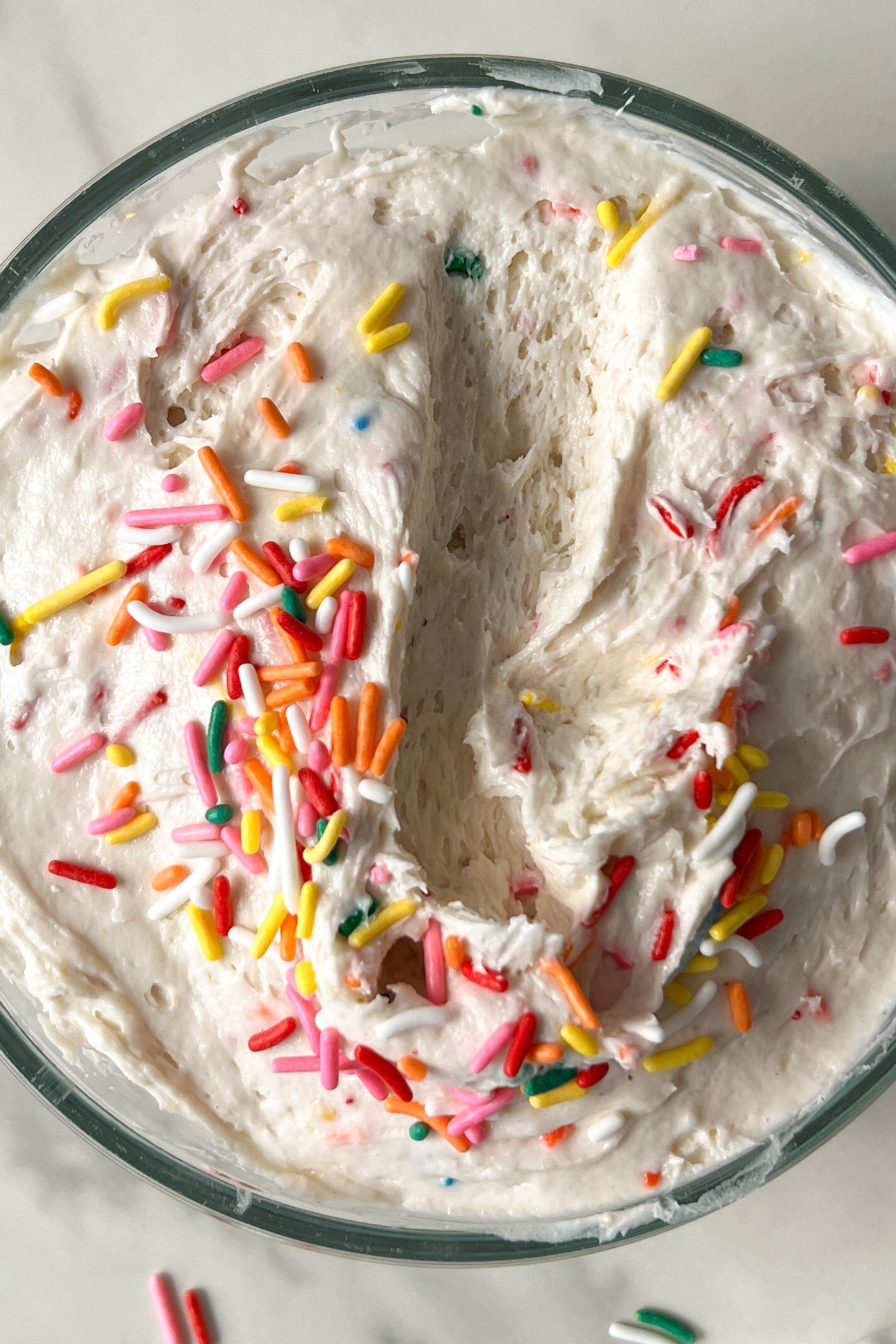 A bowl of funfetti cake dip with a scoop taken out of the middle.