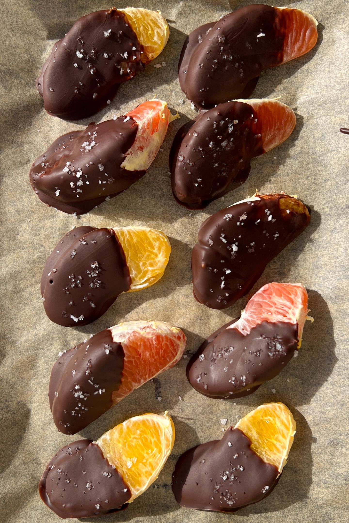 Chilled chocolate covered orange slices on parchment paper topped with sea salt flakes.
