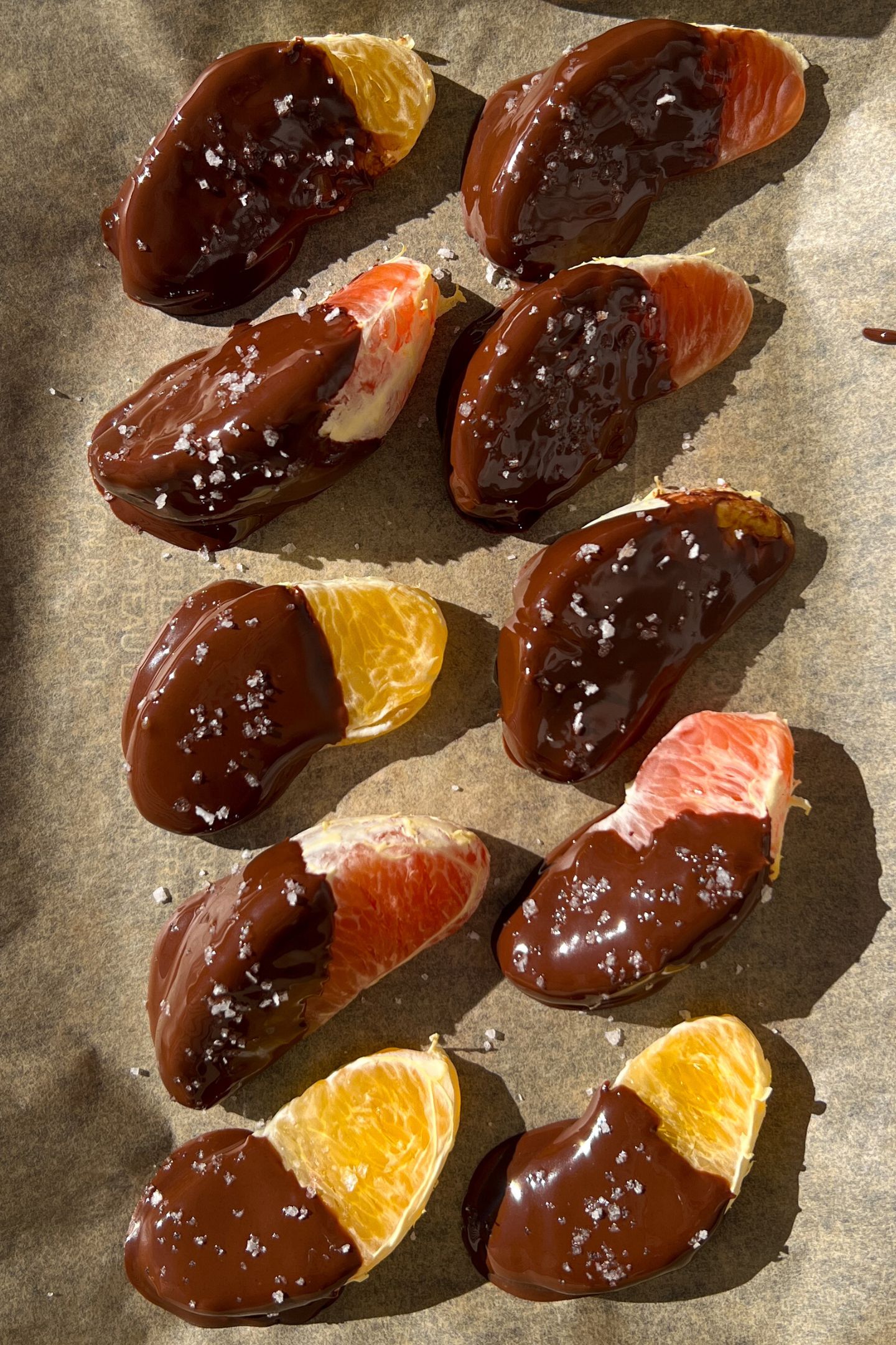 Chocolate covered orange slices on parchment paper topped with sea salt flakes.
