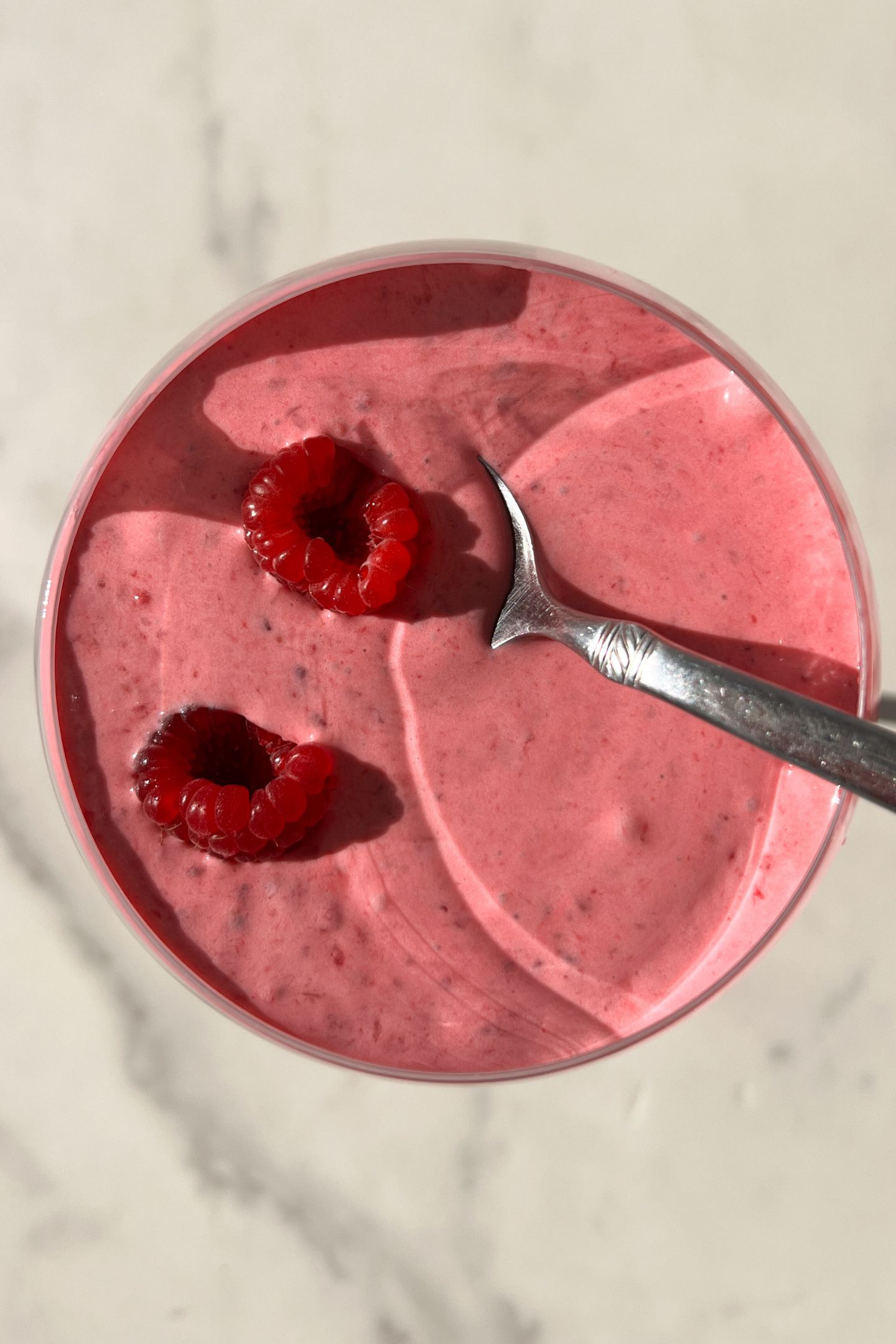 Raspberry and whipped cream in a cup with a spoon and raspberries.