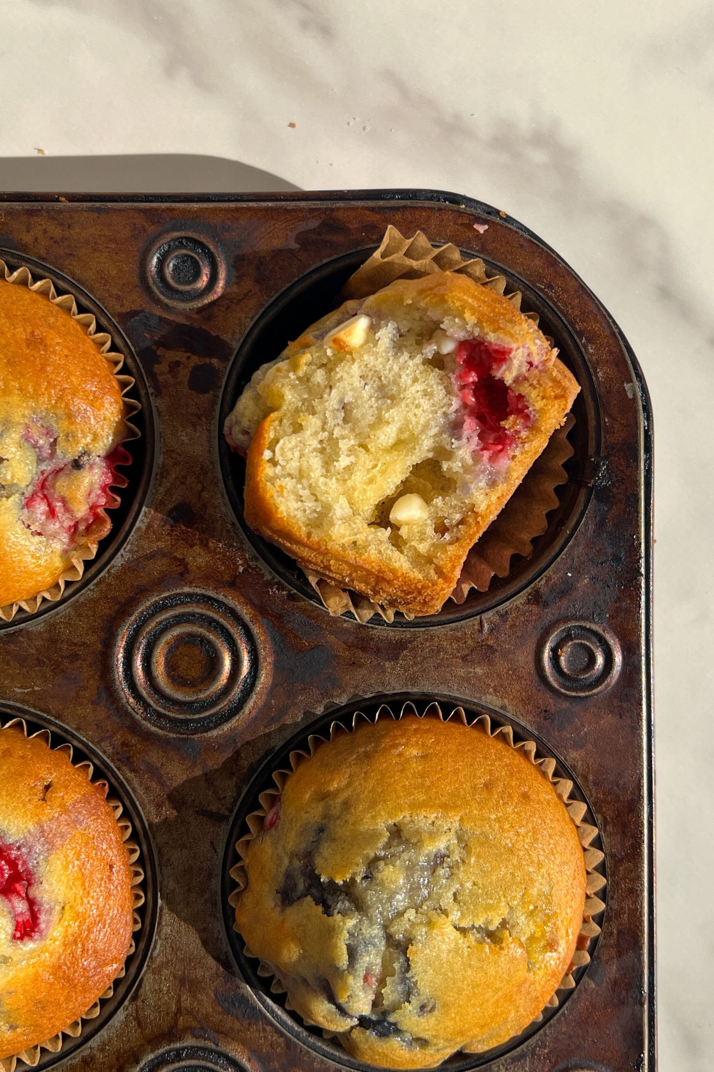 A muffin with a bite taken out of it in the muffin tin.