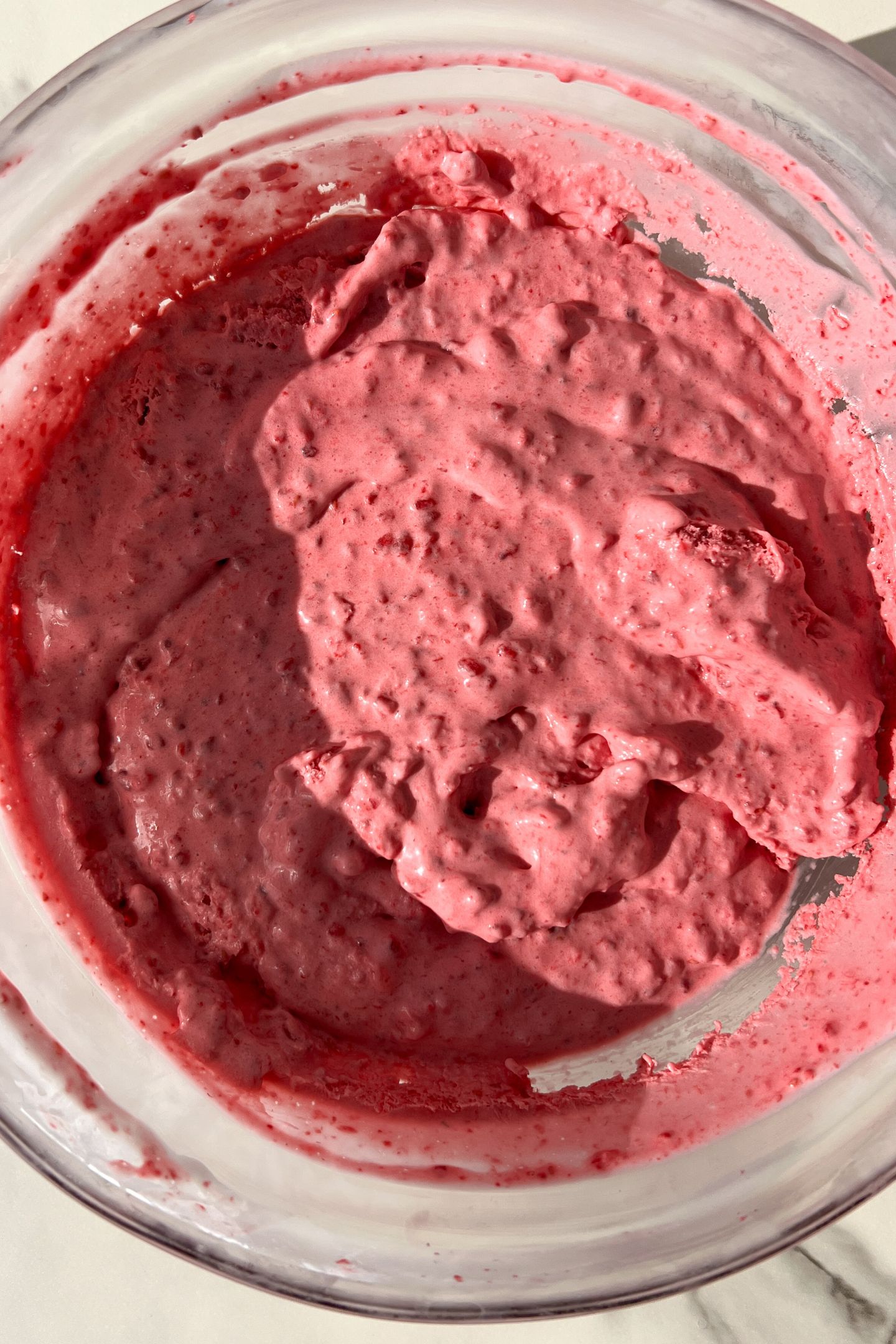 Whipped cream and the raspberry mixture combined in a bowl after being chilled in the freezer.