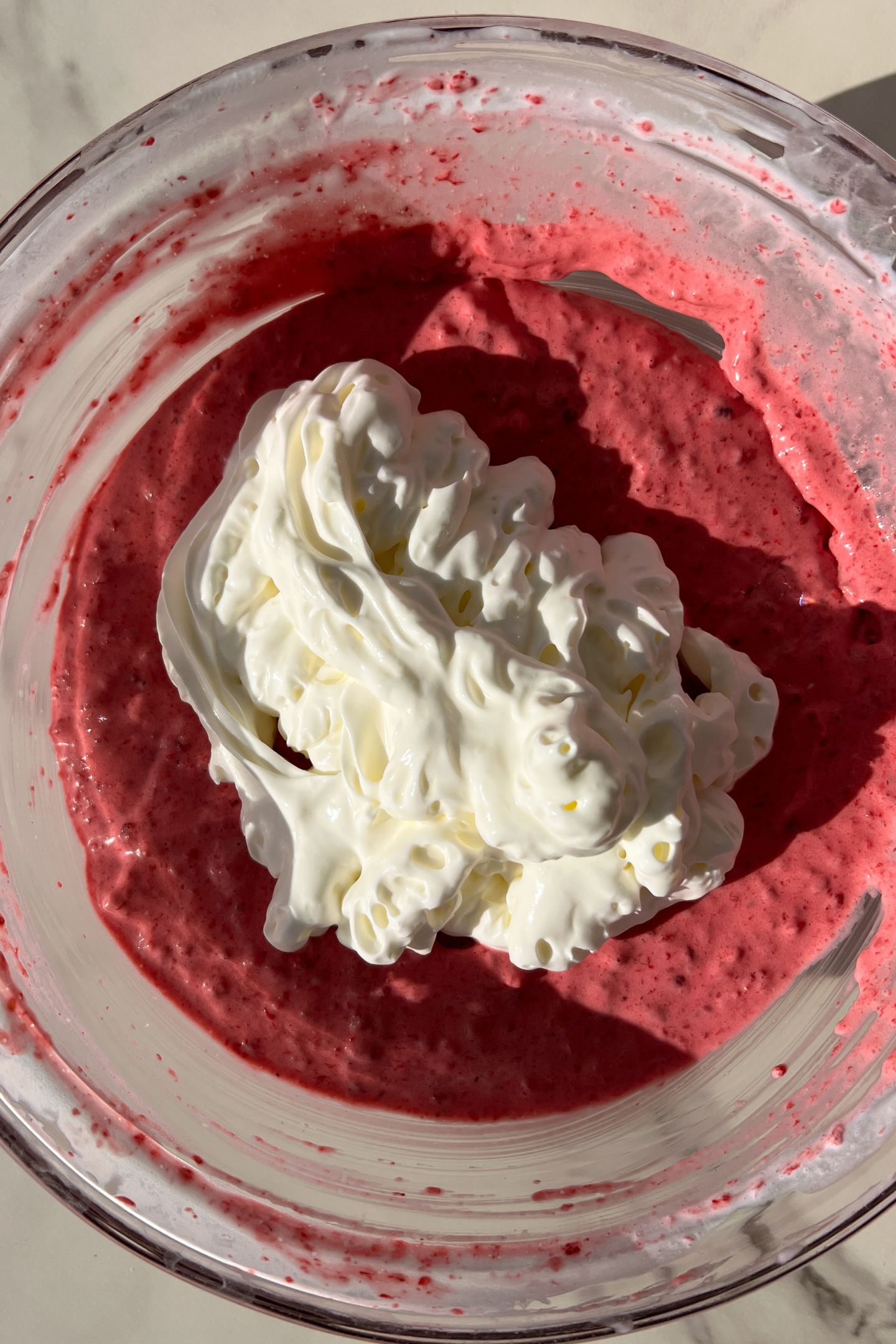 Whipped cream and the raspberry mixture in a bowl.