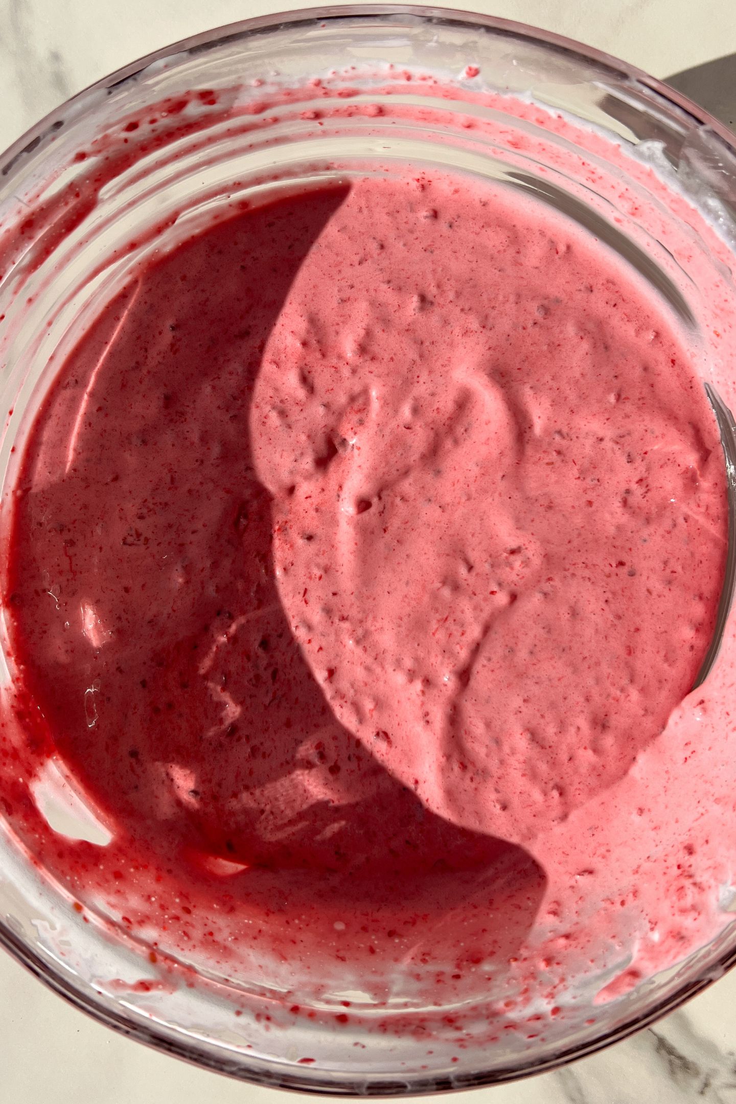 Whipped cream and the raspberry mixture combined in a bowl.