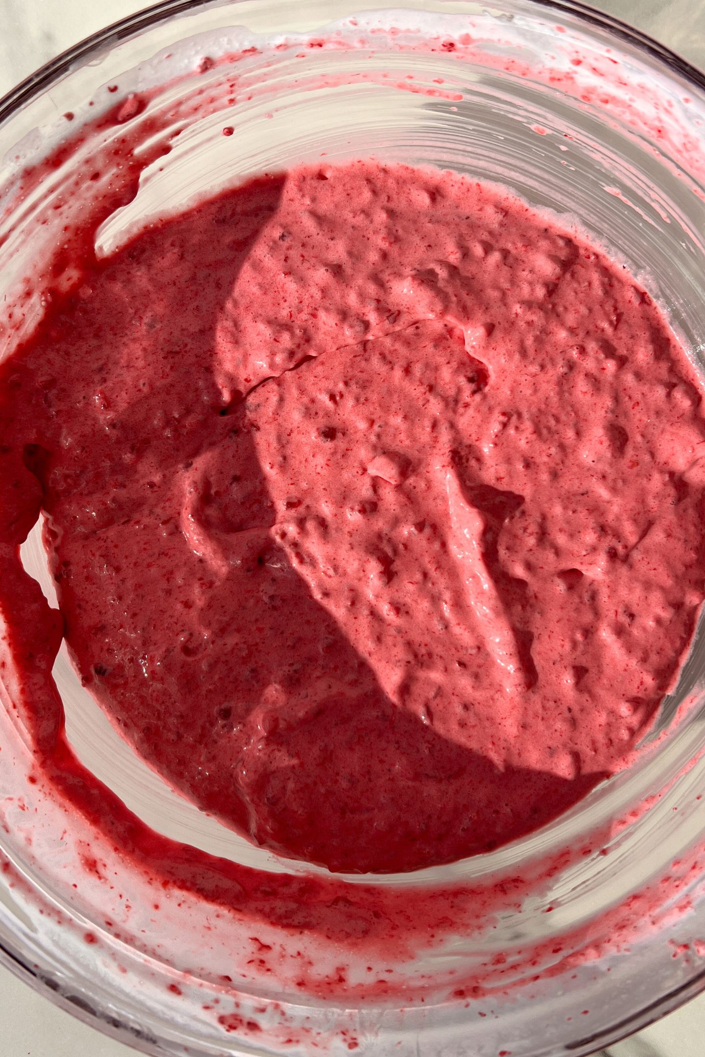 Whipped cream and the raspberry mixture combined in a bowl.