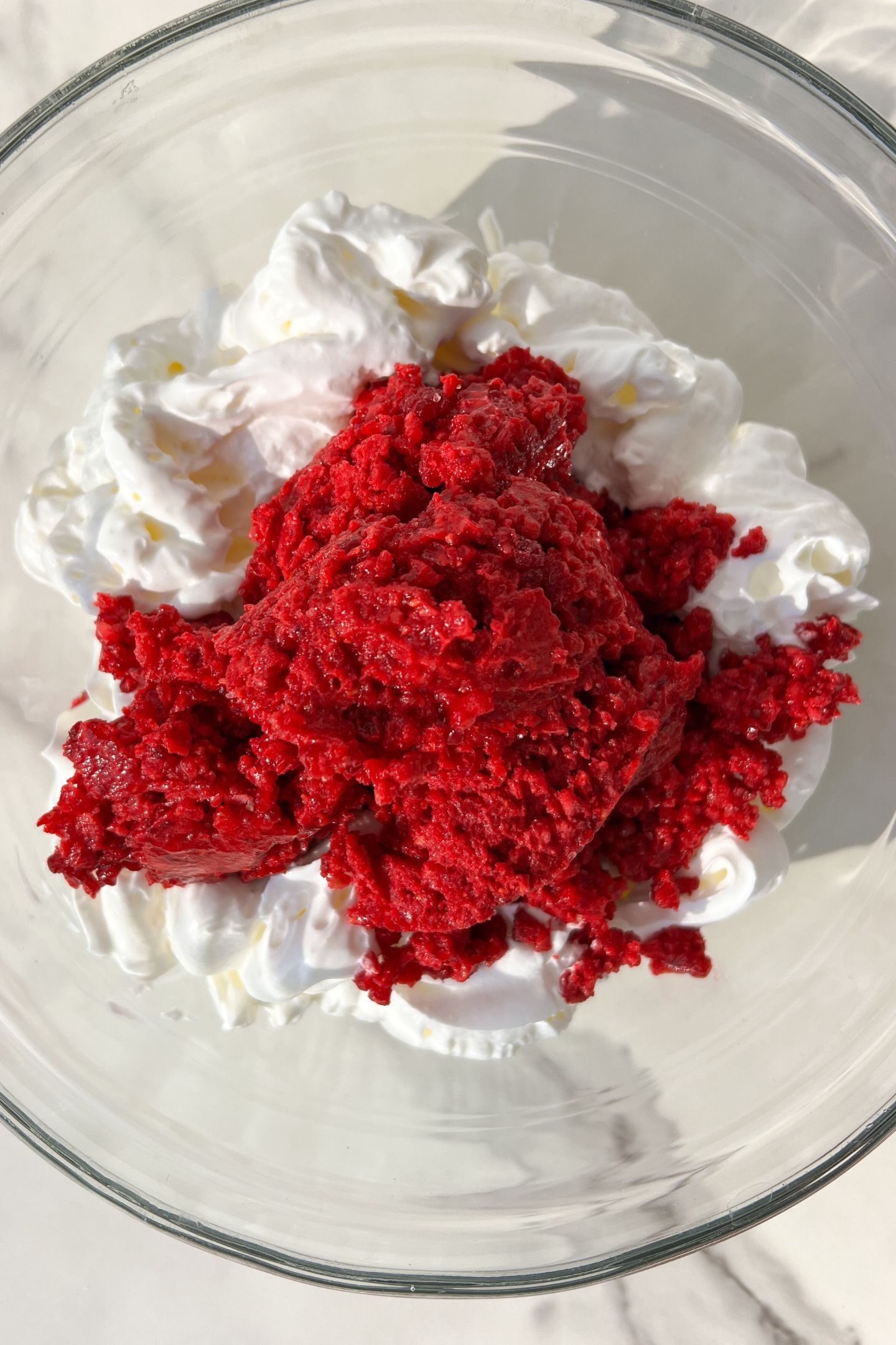 Whipped cream and the raspberry mixture in a bowl.