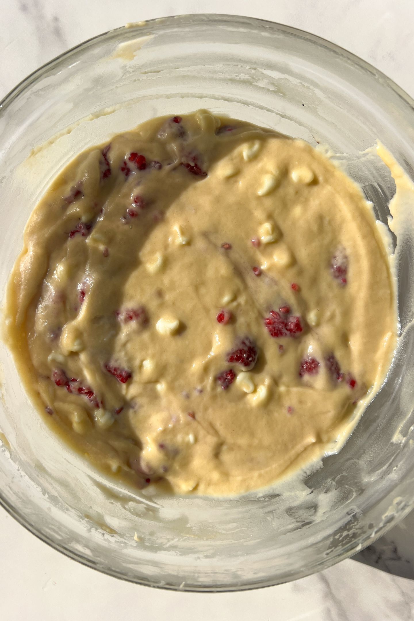 Muffin batter in a bowl mixed with the fresh raspberries and white chocolate chips.