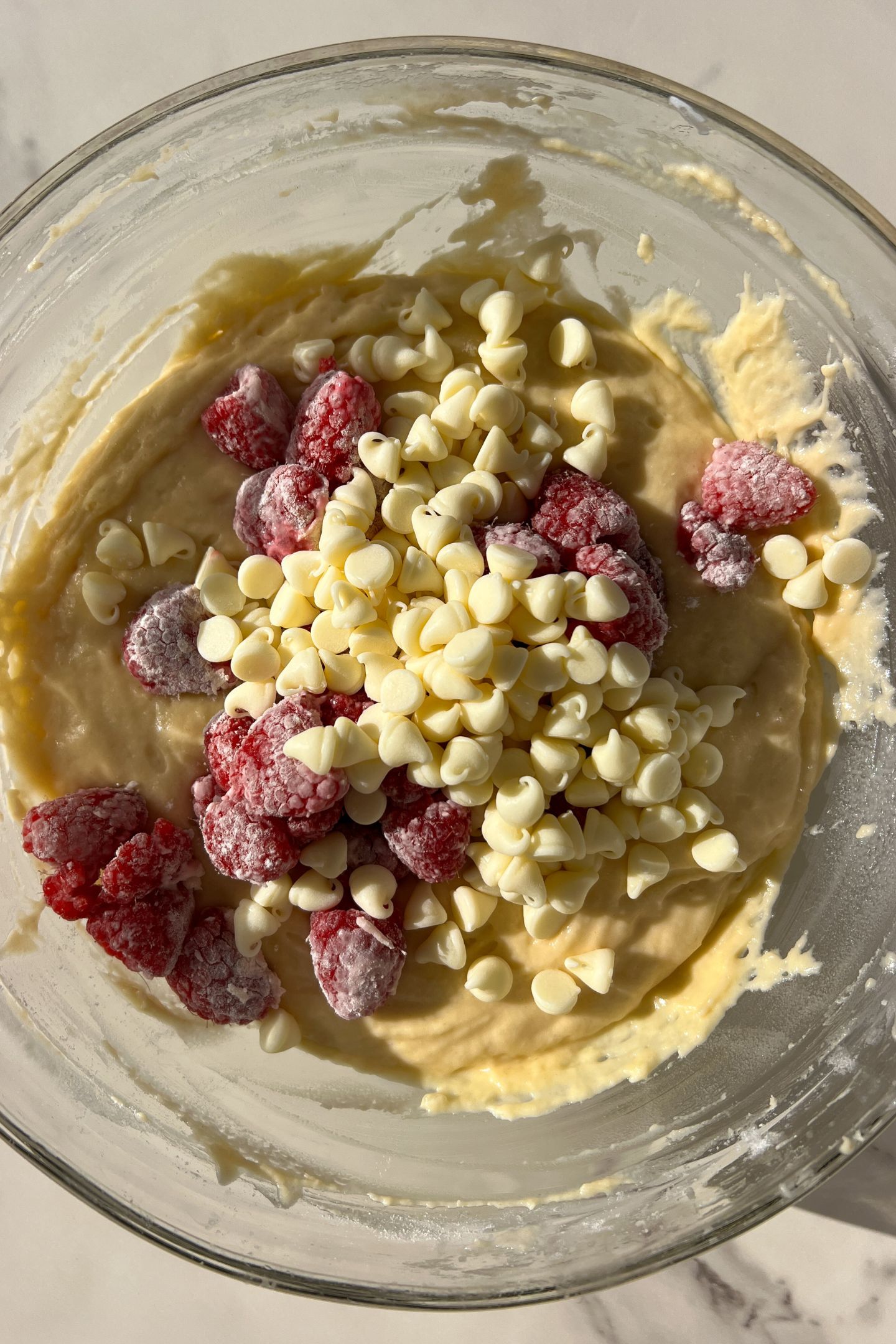 Muffin batter in a bowl topped with the fresh raspberries and white chocolate chips.