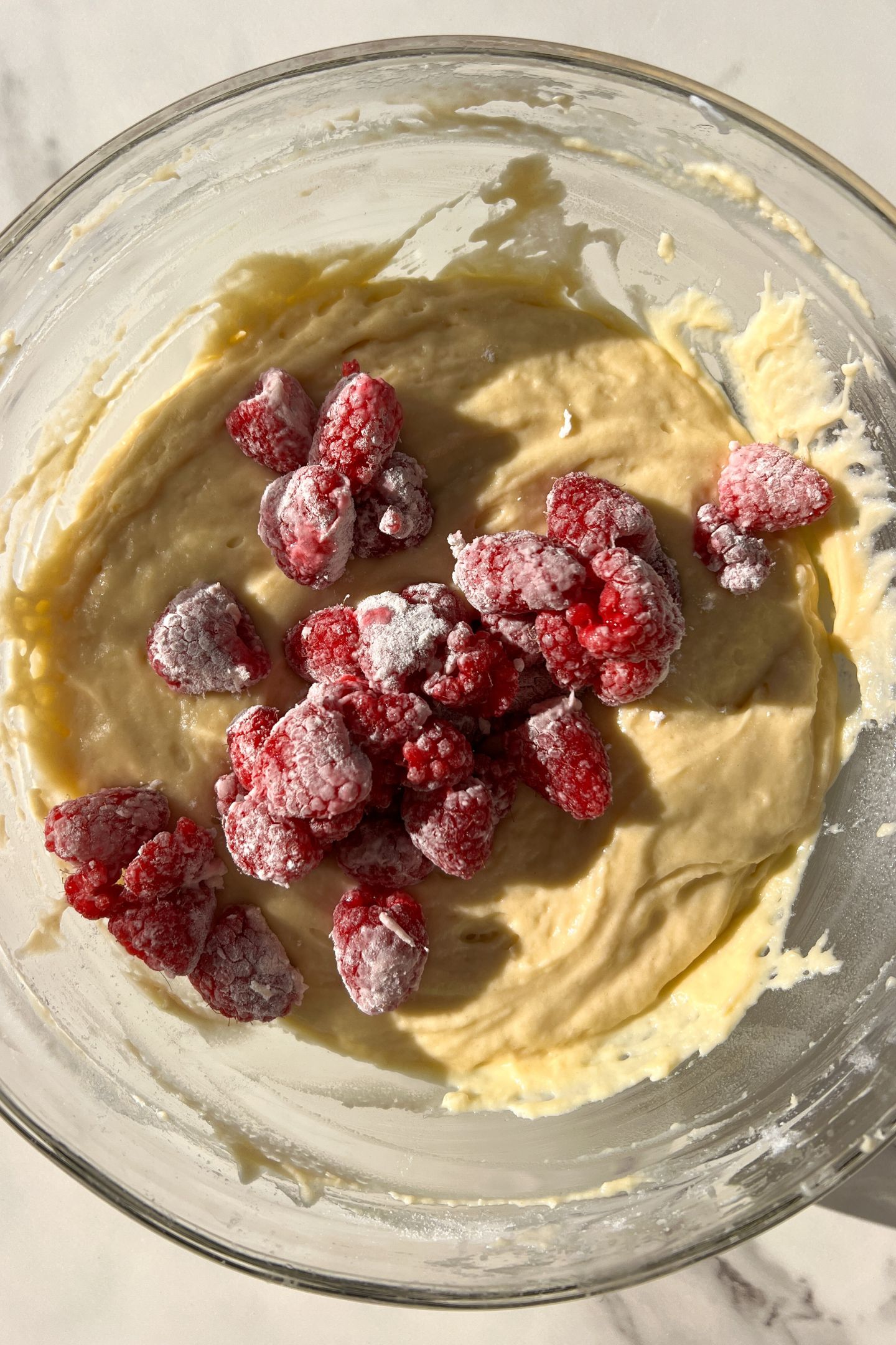 Muffin batter in a bowl topped with the fresh raspberries.