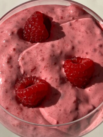 Raspberry Whipped Cream served in a glass with fresh raspberries.