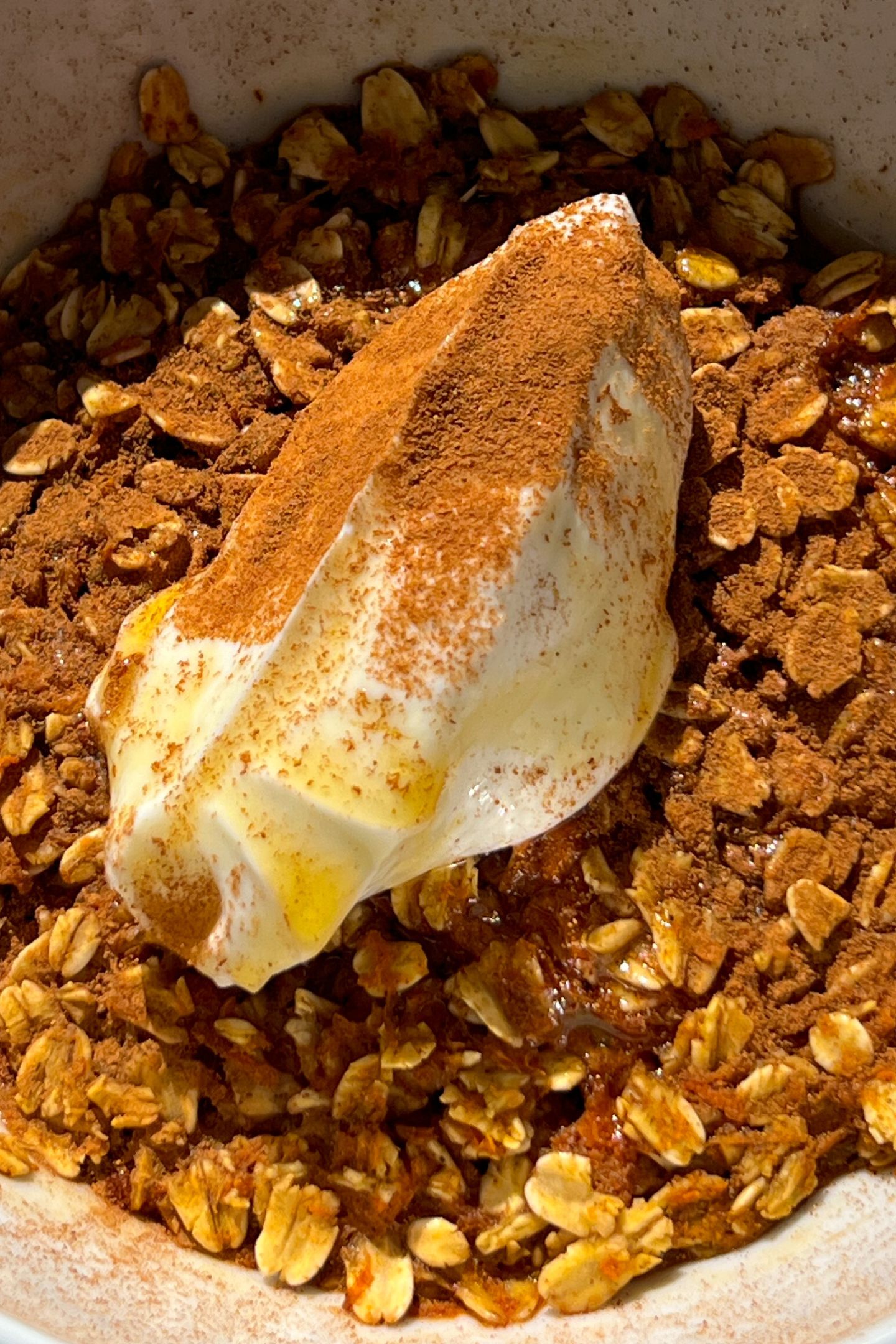 Carrot cake oatmeal in a bowl topped with yogurt, cinnamon and maple syrup.