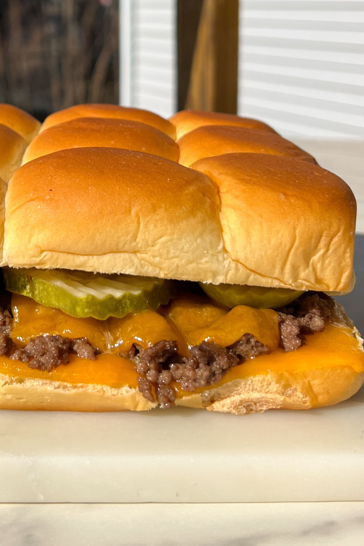 Cheeseburger slider with melted cheese and a pickle on Hawaiian roll.