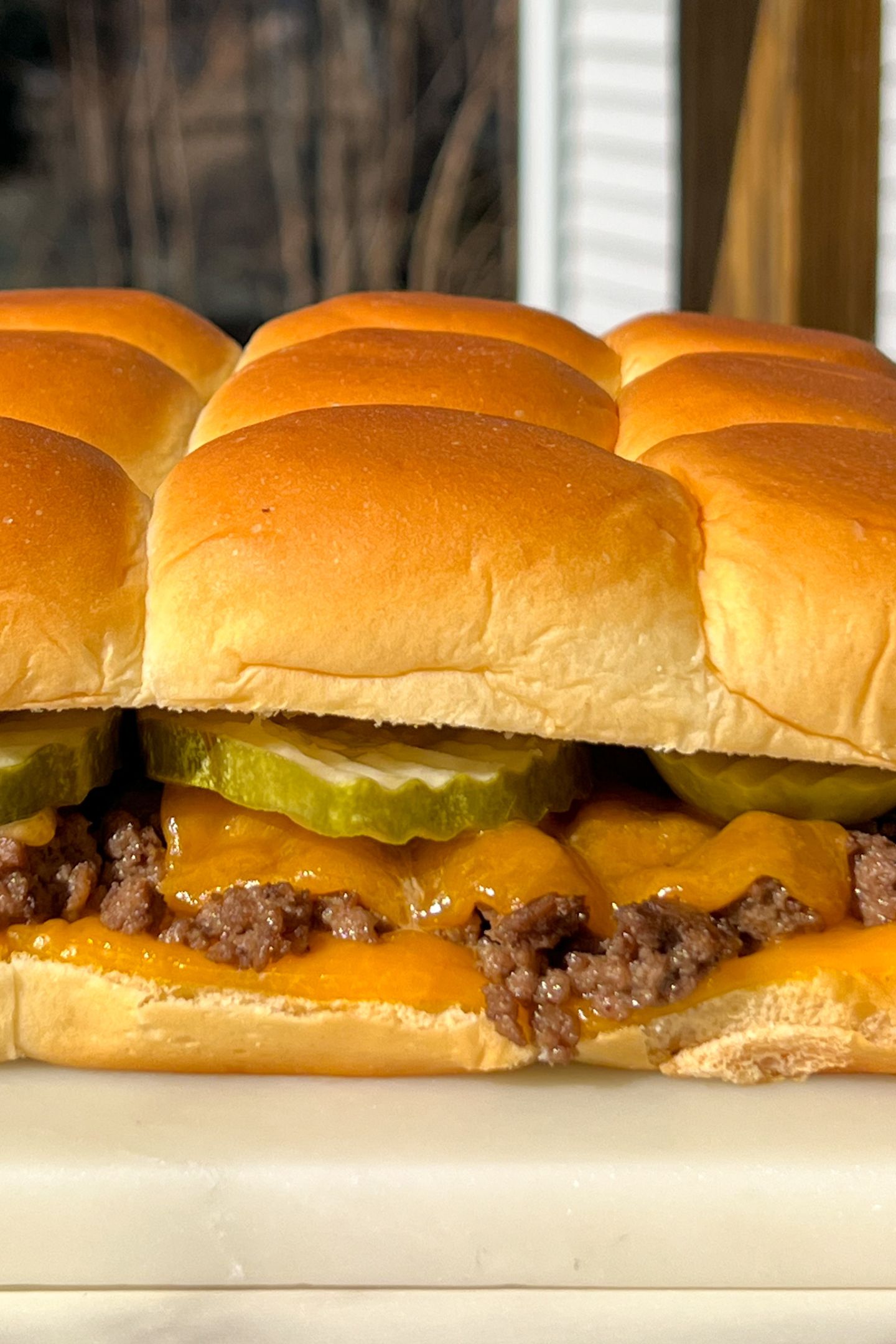 Cheeseburger slider with melted cheese and a pickle on Hawaiian roll.