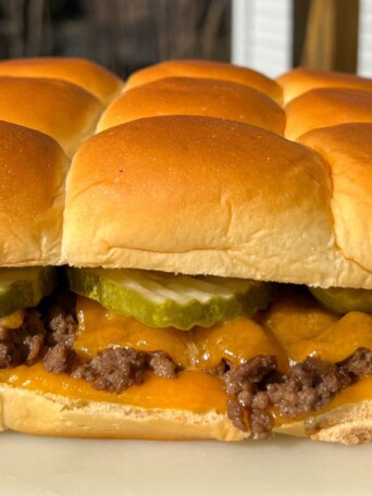 Cheeseburger slider with melted cheese and a pickle on Hawaiian roll.