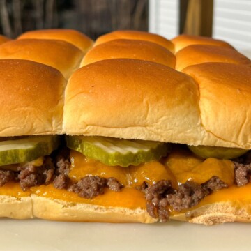 Cheeseburger slider with melted cheese and a pickle on Hawaiian roll.
