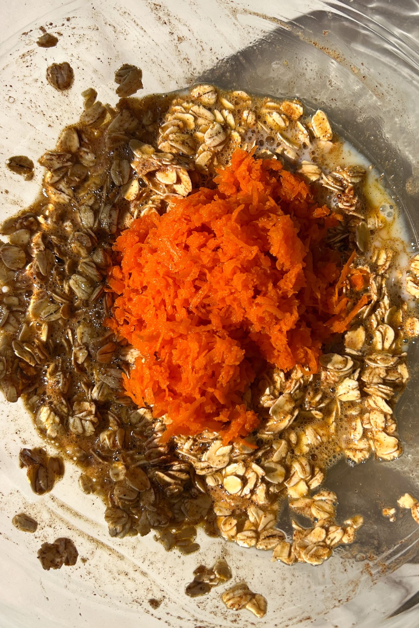 Liquid and dry ingredients in bowl with shredded carrots.
