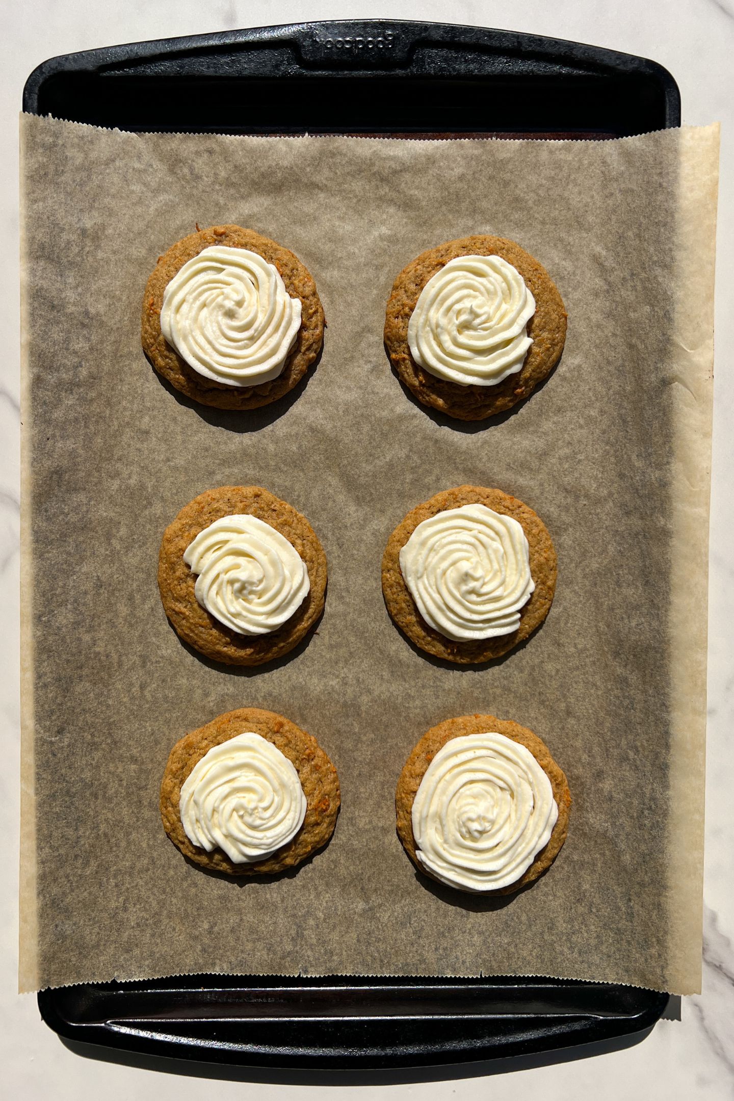 Carrot cake cookies topped with cream cheese frosting on a baking sheet.
