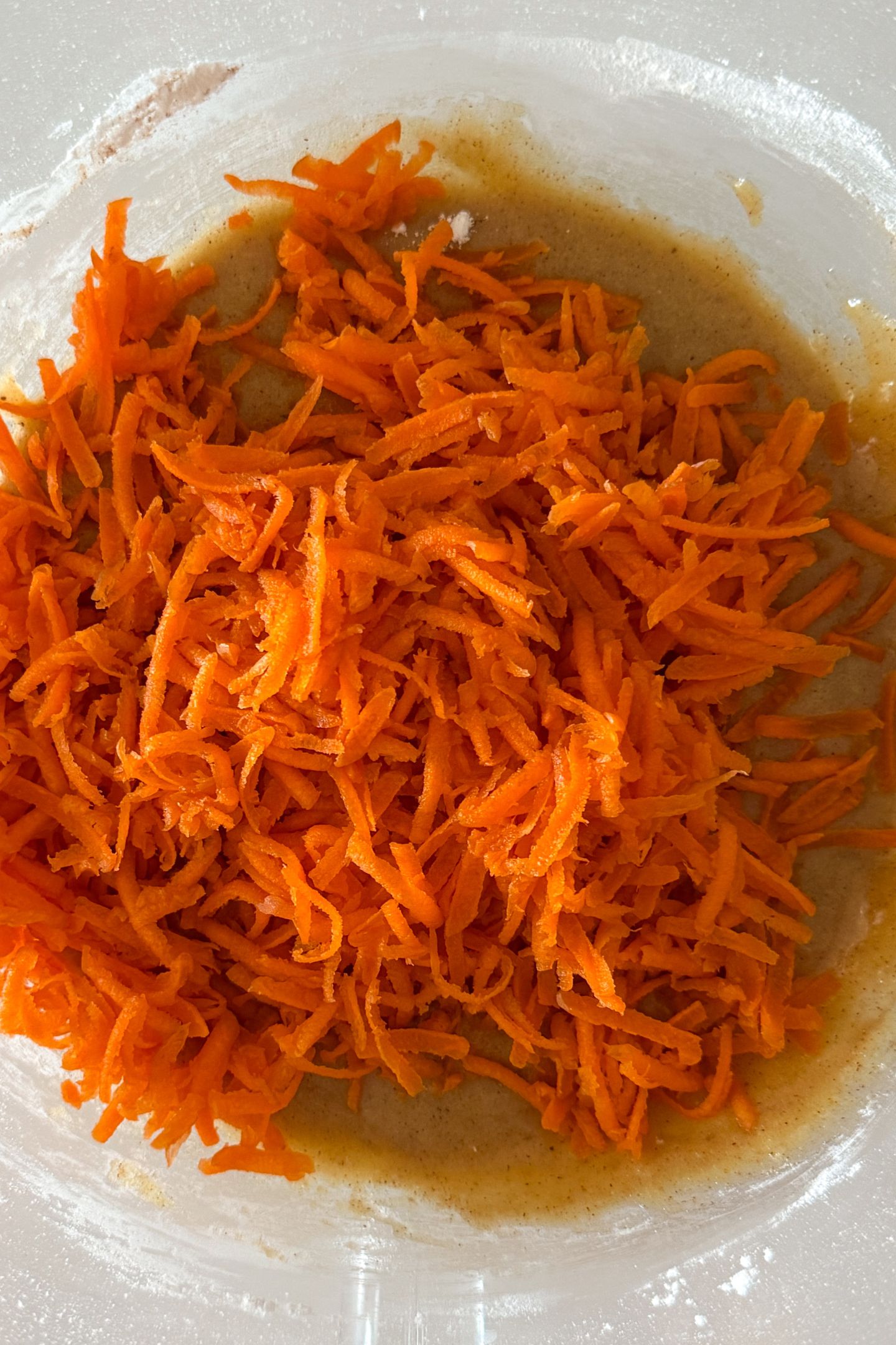 Shredded carrots being added to the wet ingredients in a mixing bowl.