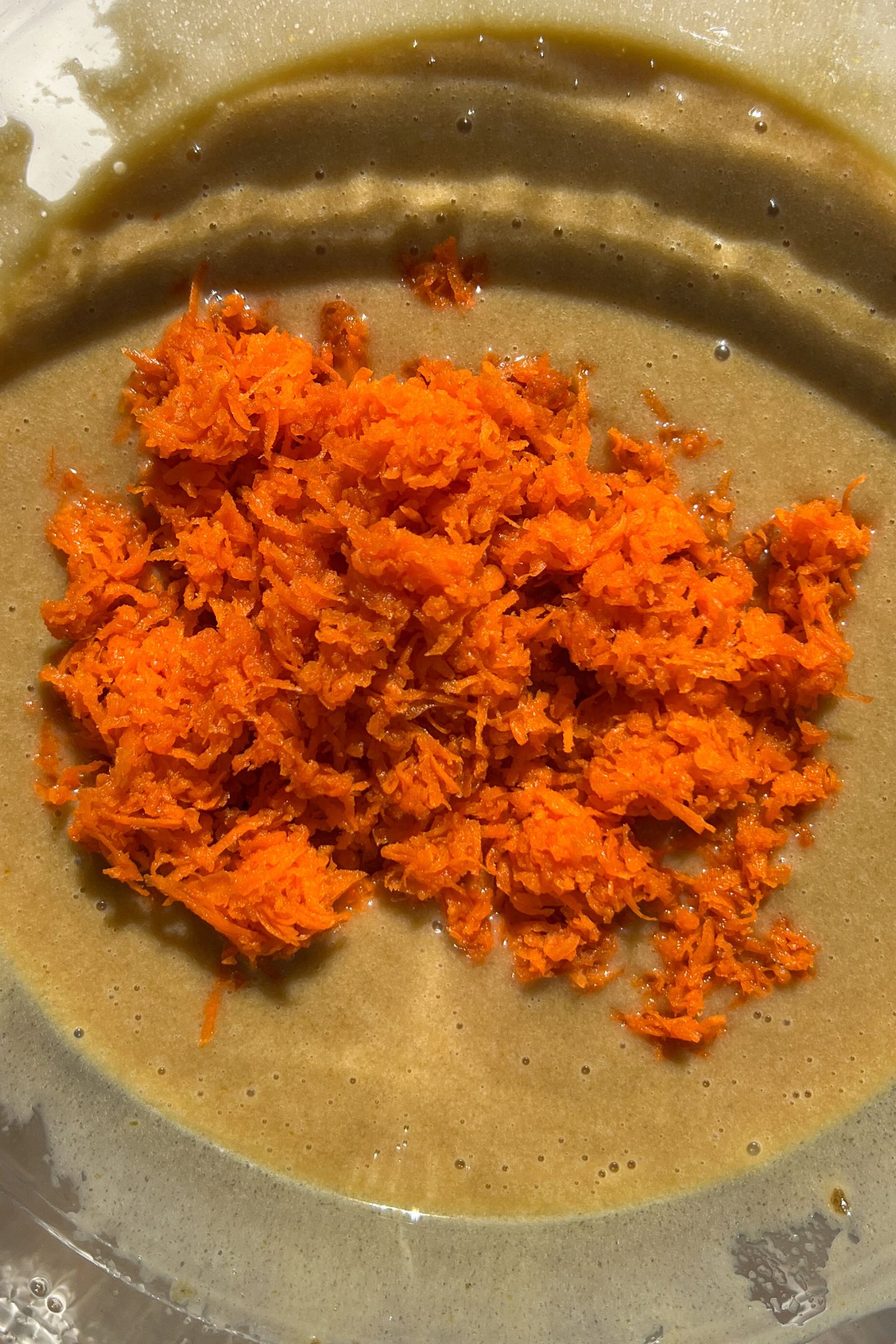 Wet ingredients in mixing bowl with grated carrots.