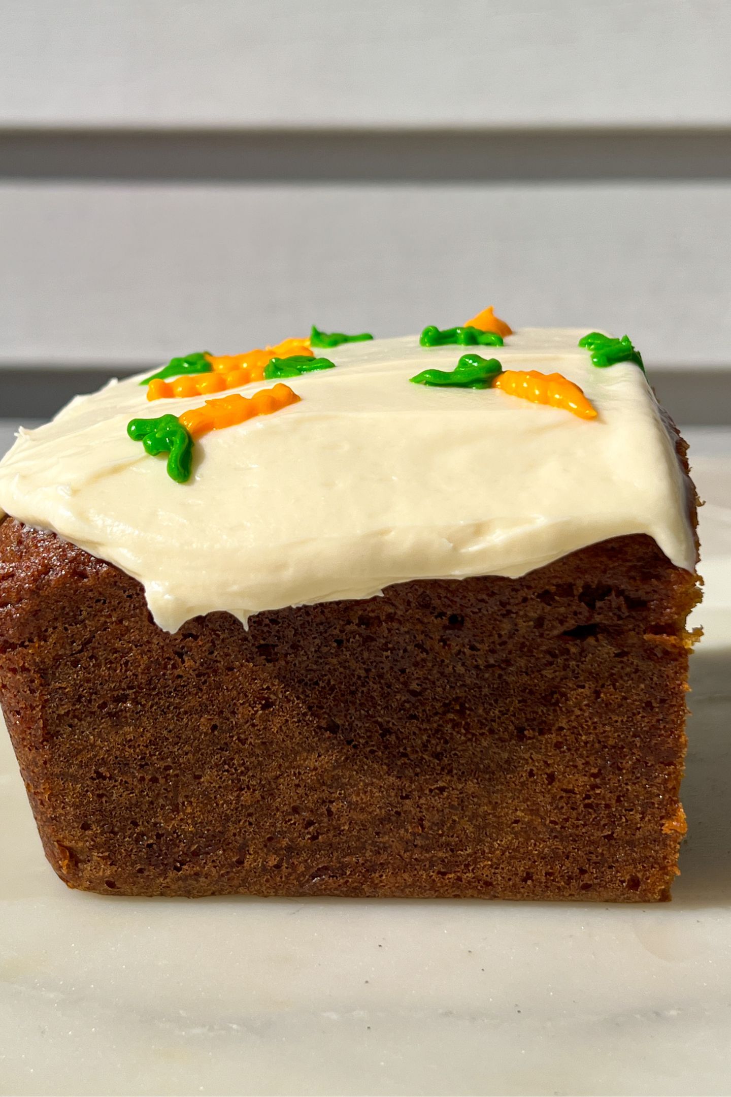 A side view of Frosted carrot cake loaf with carrot frosted decorations on top.
