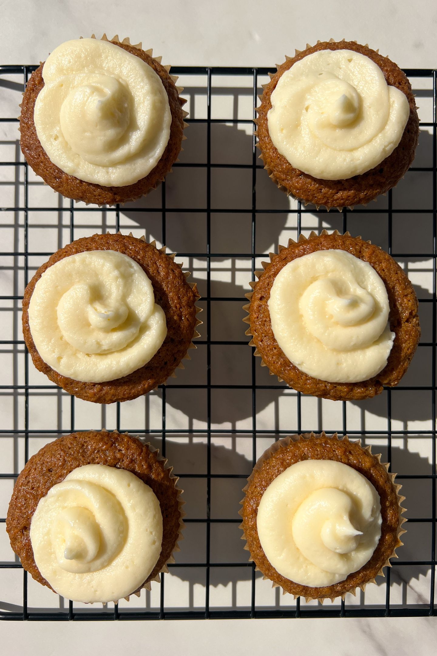 Cooled Carrot Cake Cupcakes in cupcakes liners on cooling rack topped with cream cheese frosting.