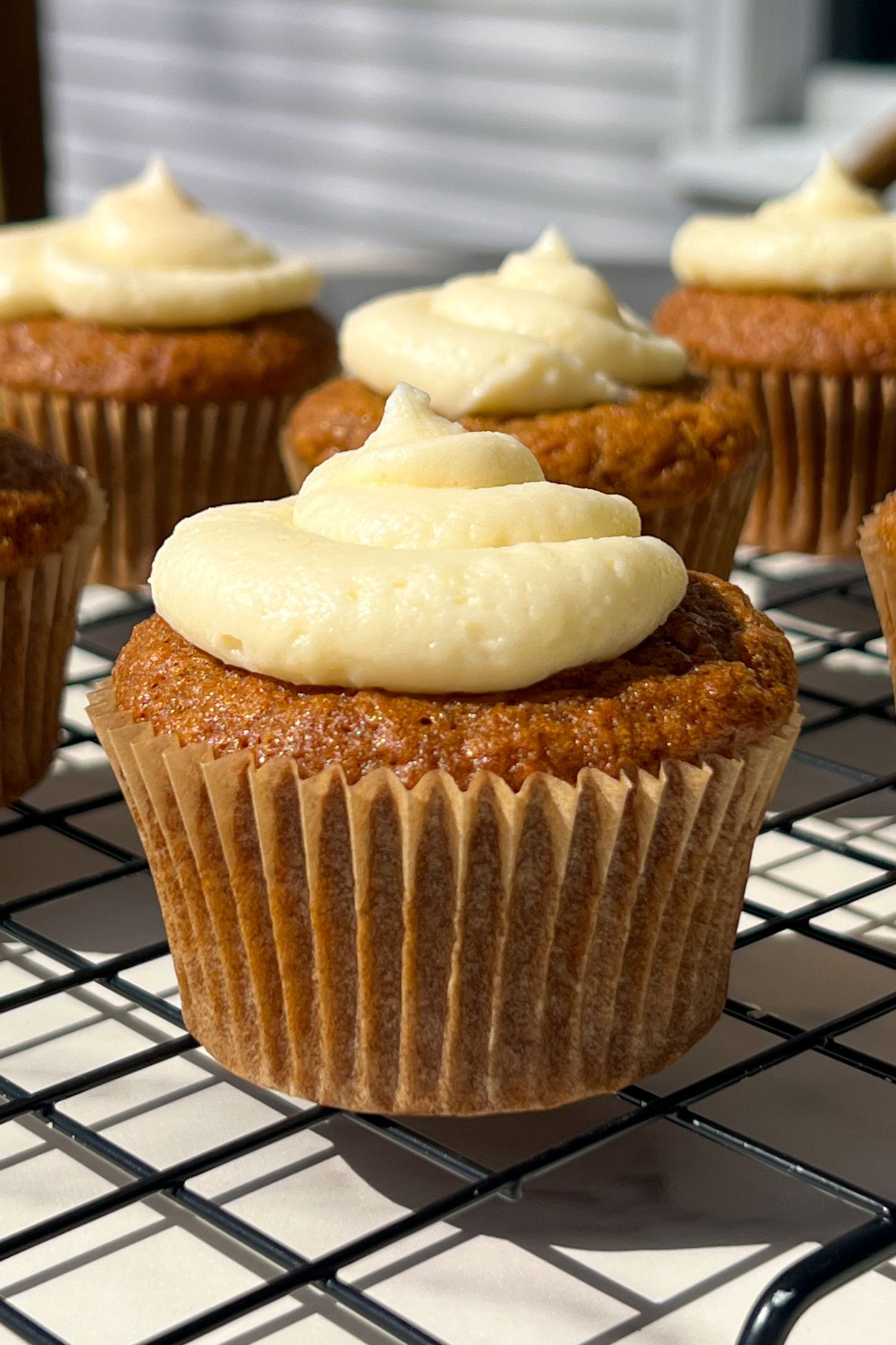 Cooled Carrot Cake Cupcakes in cupcakes liners on cooling rack topped with cream cheese frosting.