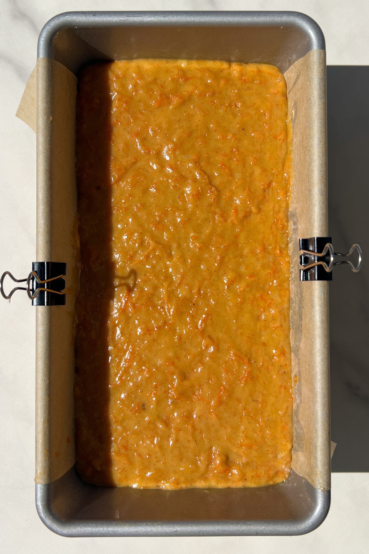Carrot cake batter in a loaf pan lined with parchment paper. 