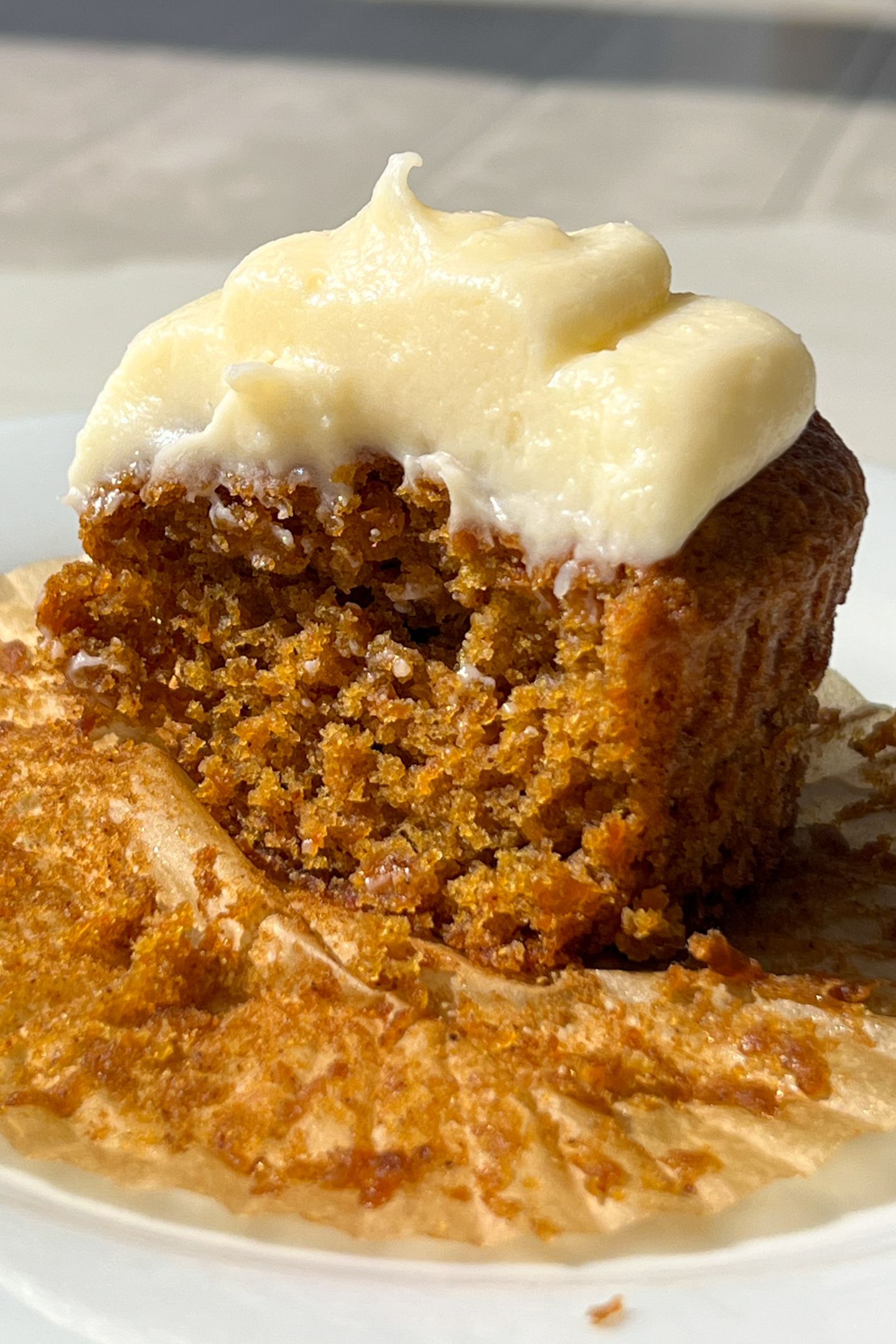 A Gluten Free Carrot Cake cupcake with frosting and a bite taken out of it.