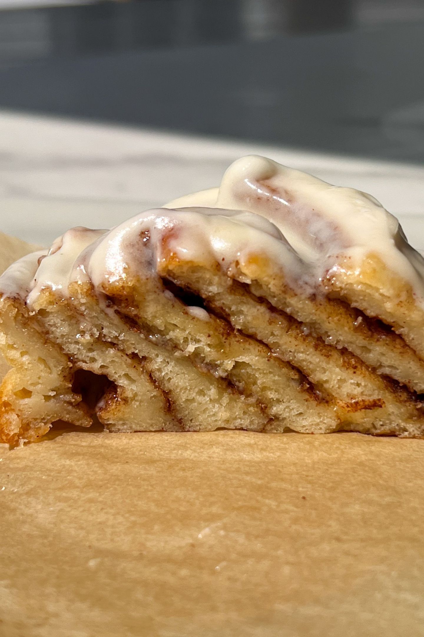 A cinnamon roll on parchment paper topped with frosting and cut in half.