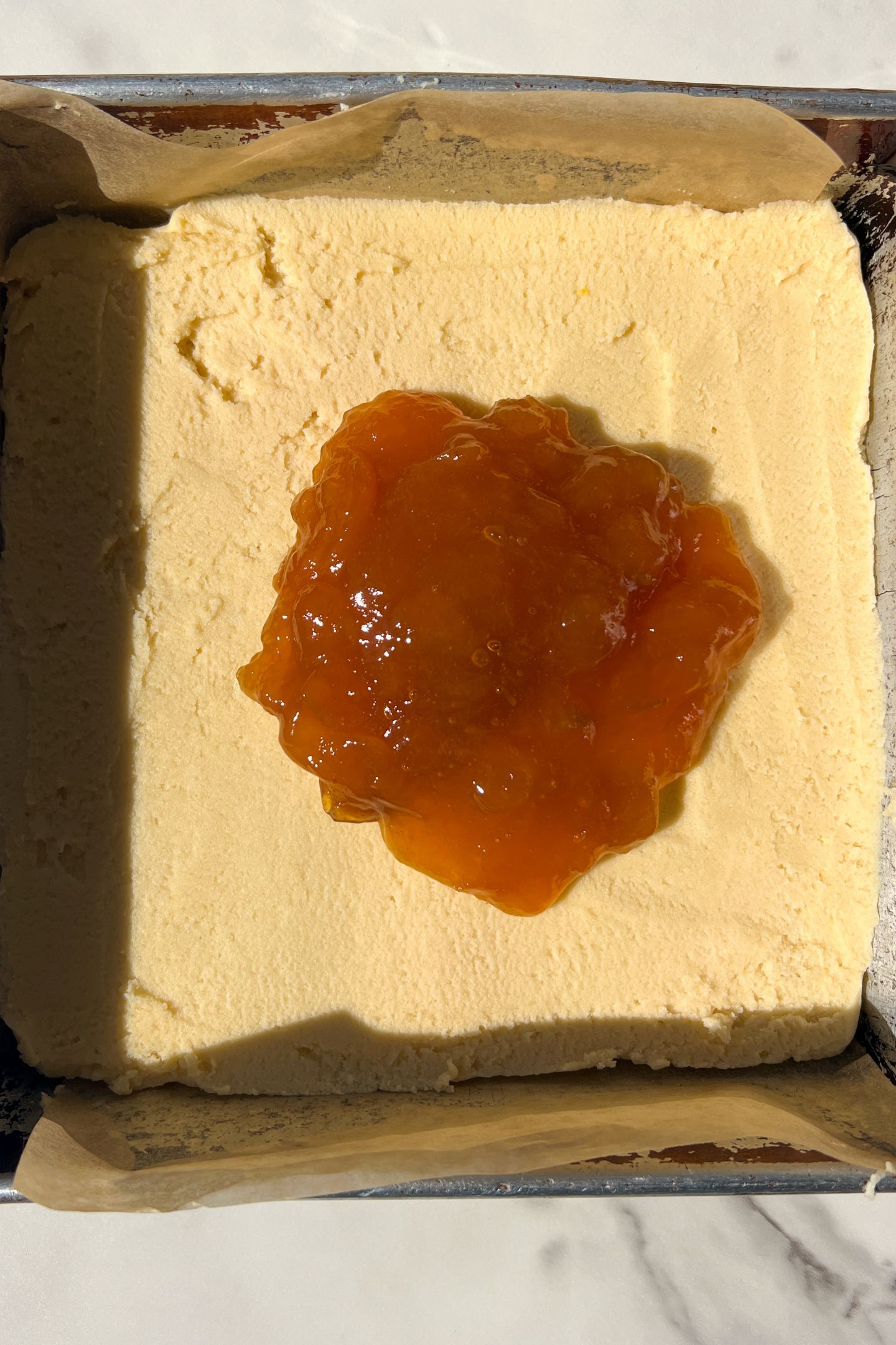 Dough spread into a greased 8x8 square pan lined with parchment and topped with the Apricot Jam.