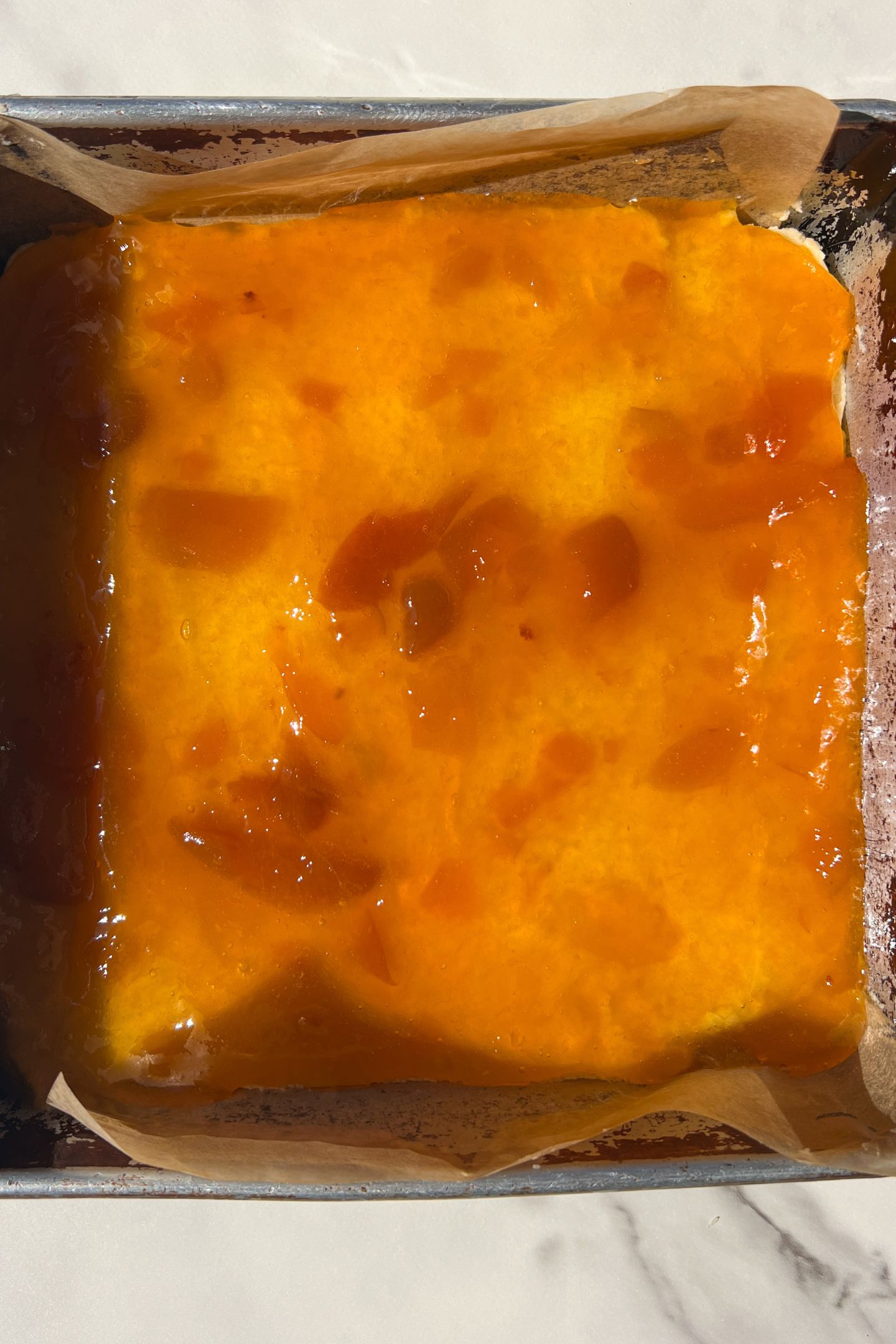 Dough spread into a greased 8x8 square pan lined with parchment and topped with the Apricot Jam spread in an even layer.