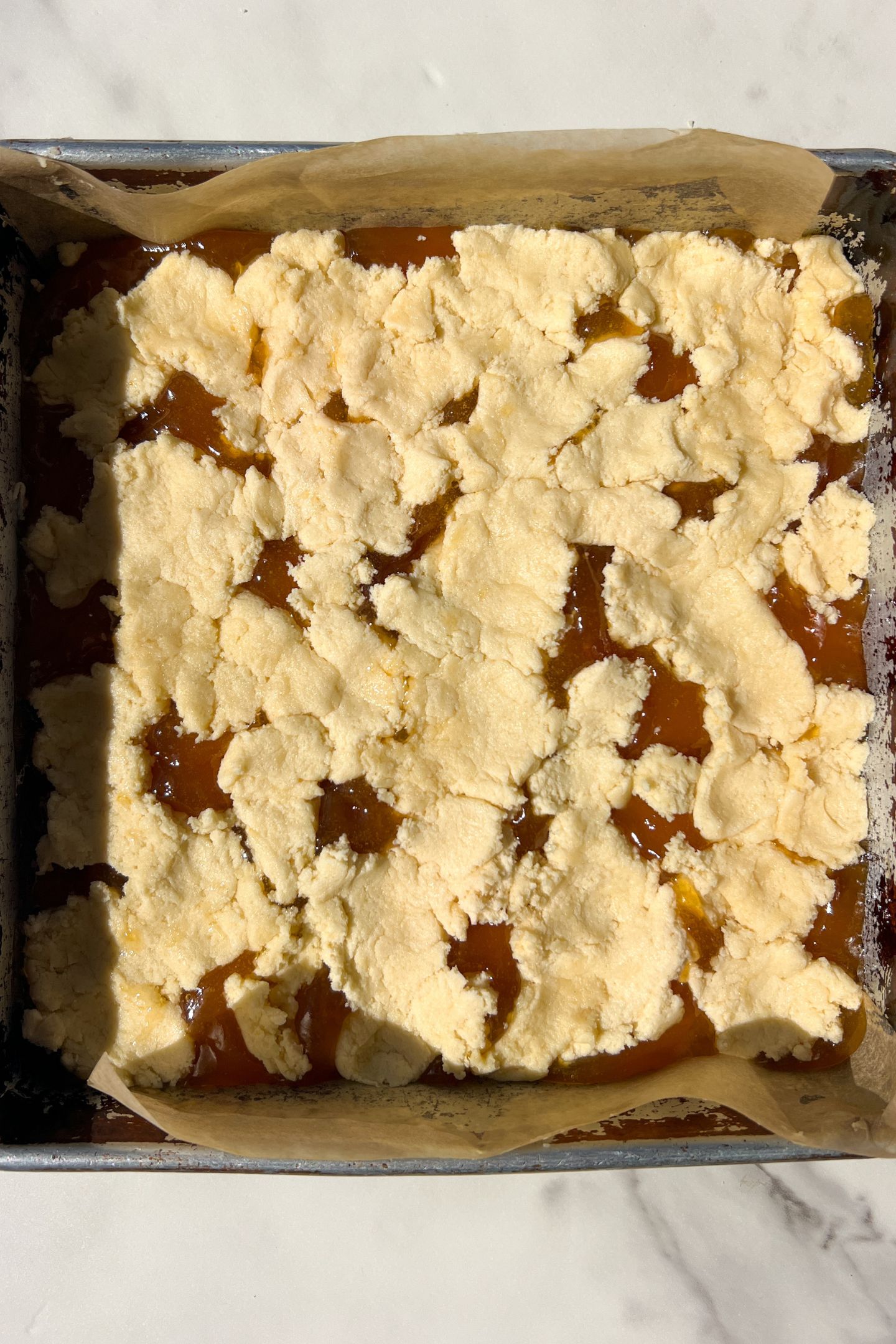 Clumps of dough added on top of the apricot jam in the baking pan.