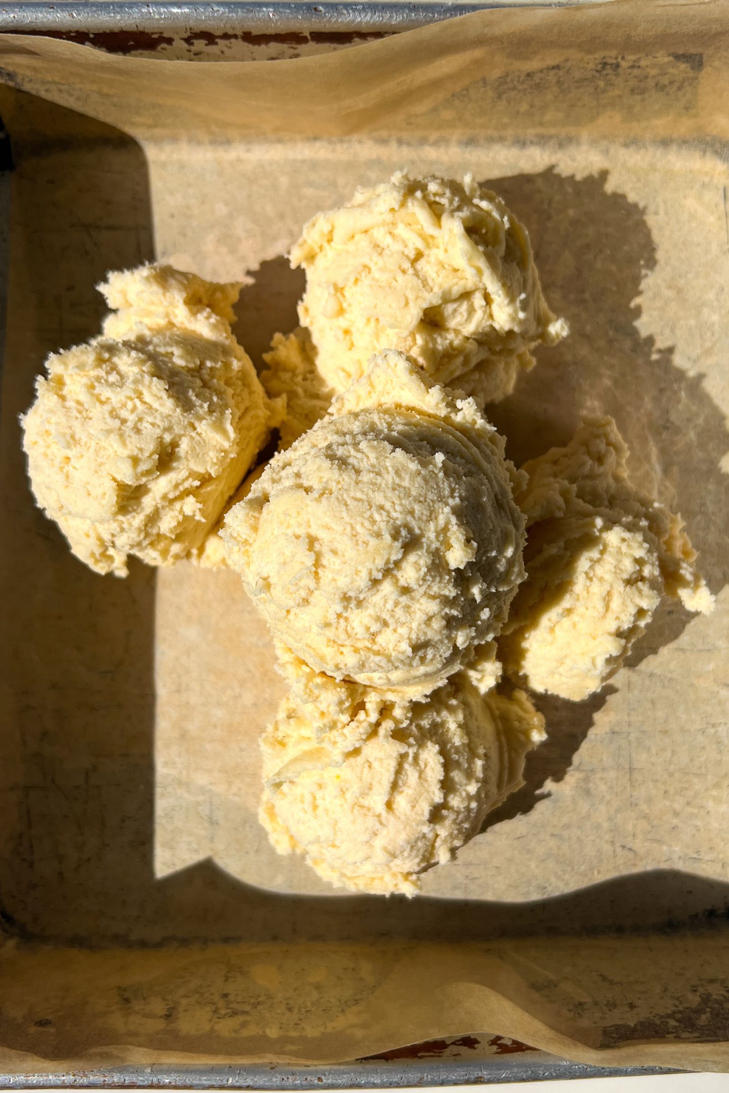 Dough being added to a greased 8x8 square pan lined with parchment.
