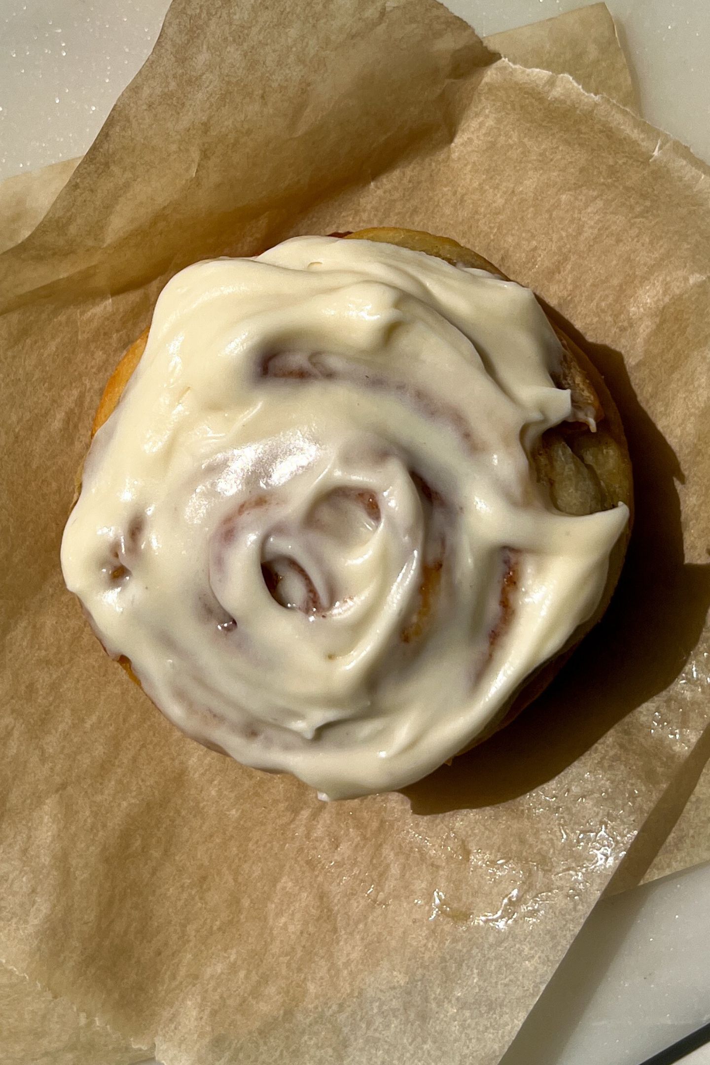 Baked cinnamon roll on parchment paper topped with frosting.