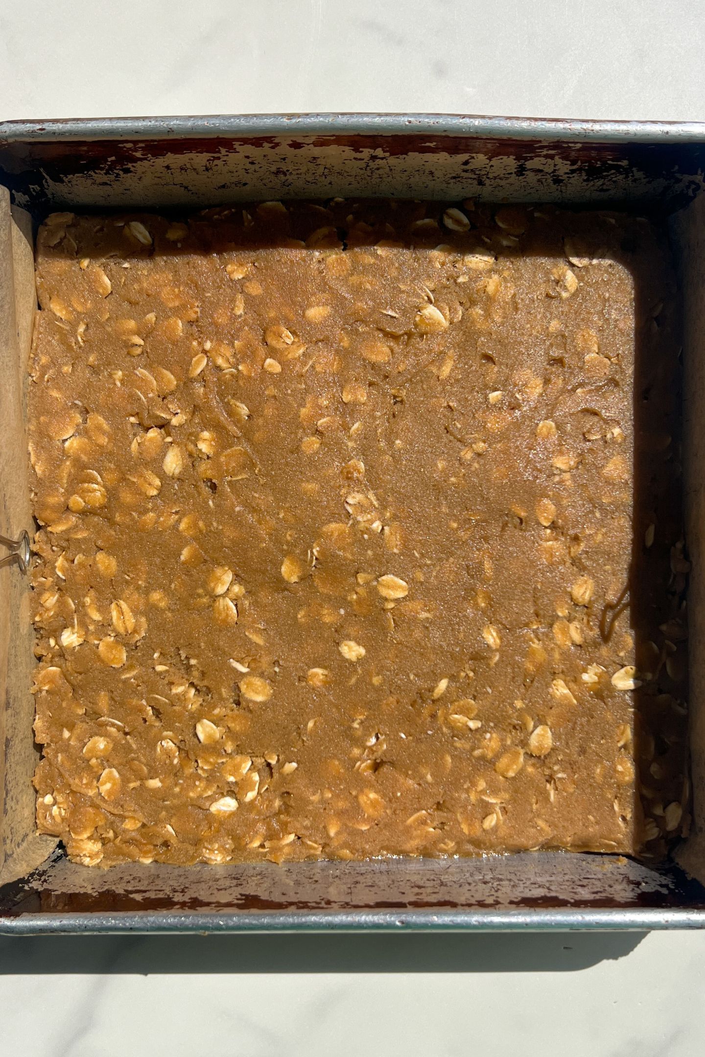 Oatmeal cookie base dough pressed into a prepared baking pan.