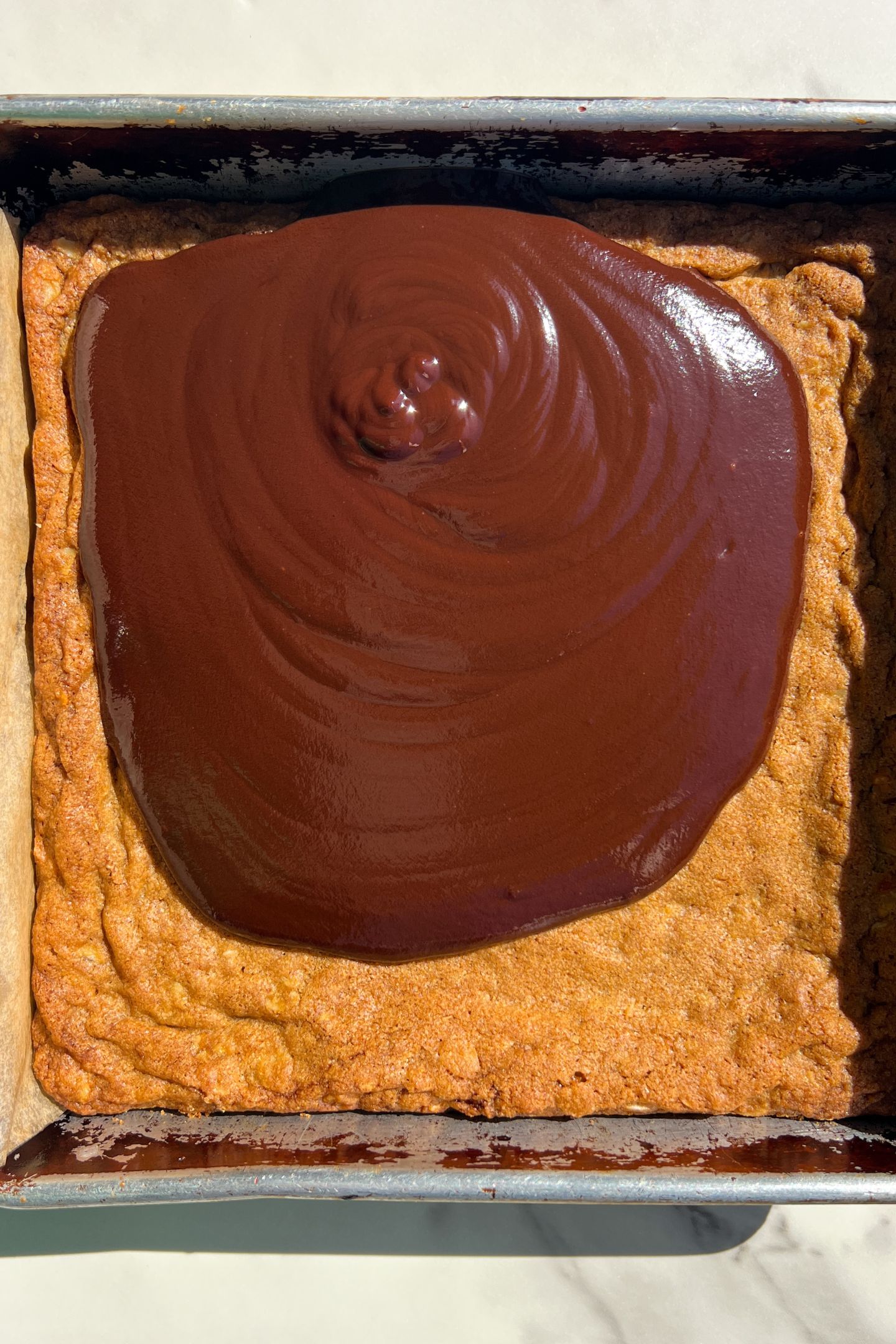 Baked oatmeal cookie base in pan topped with chocolate ganache.