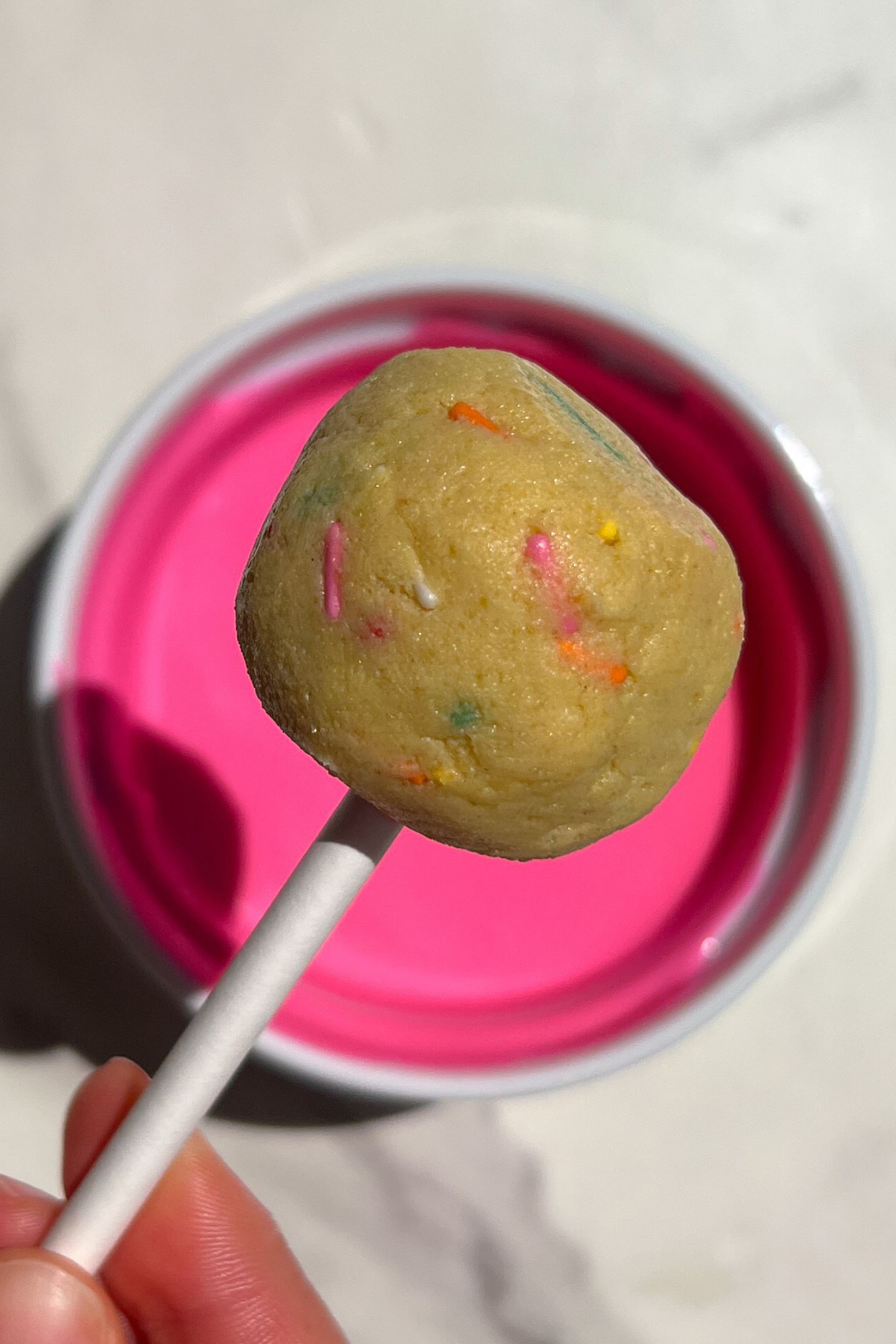 Holding cake pop over chocolate. 