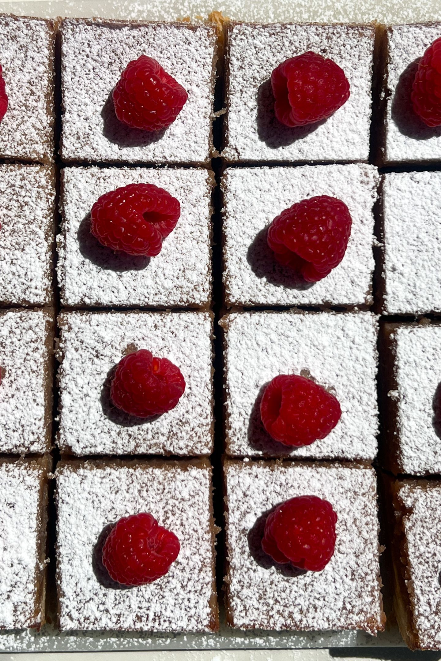 Sliced Raspberry and Lemon Bars with powdered sugar and fresh raspberries on top.