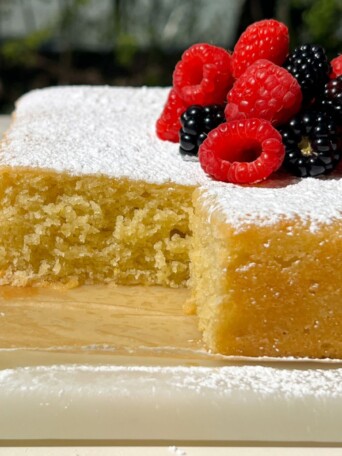 Lemon Olive Oil Cake topped with powdered sugar and berries with a slice taken out of it.