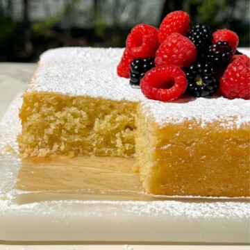 Lemon Olive Oil Cake topped with powdered sugar and berries with a slice taken out of it.
