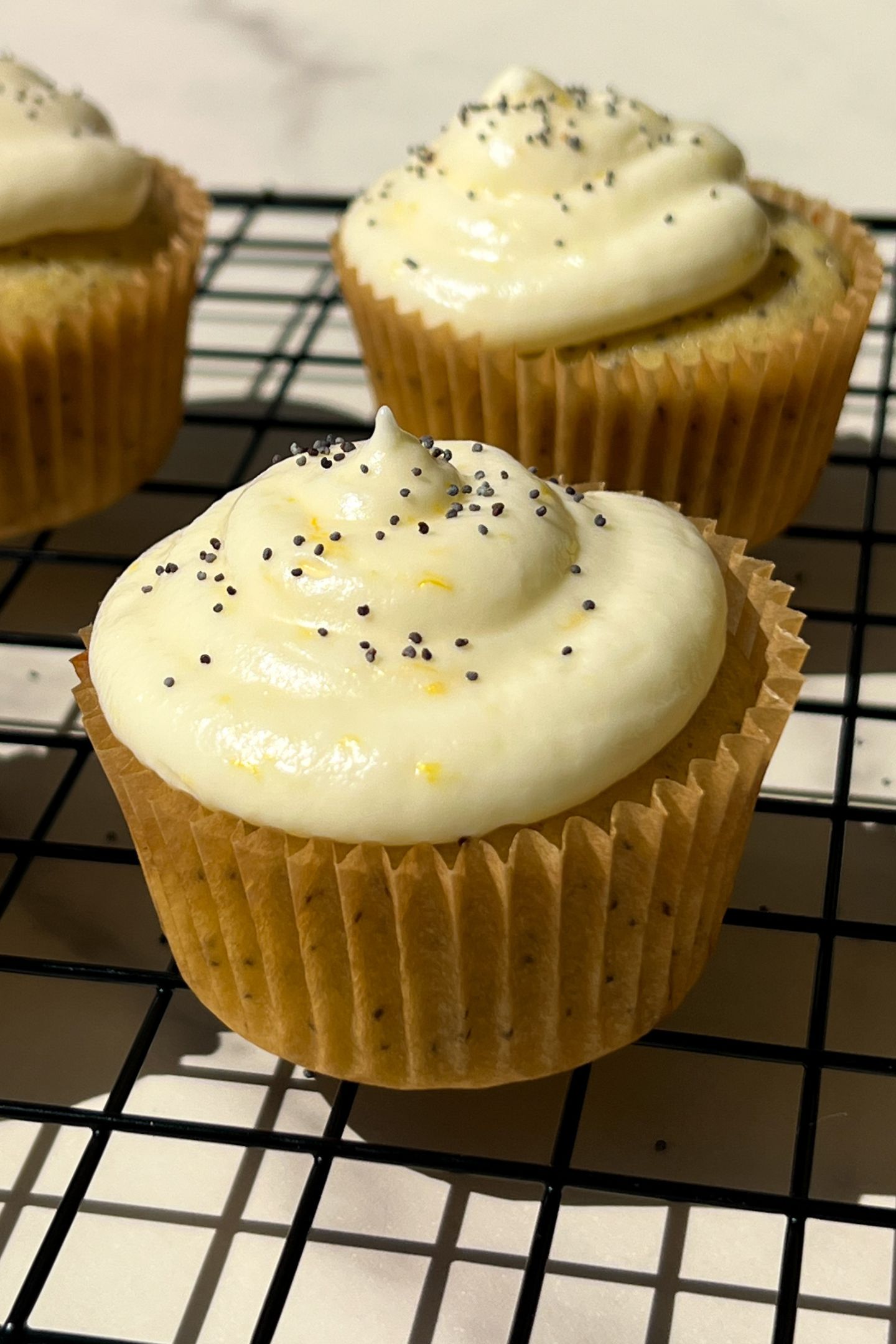 Decorated lemon poppy seed cupcake on a cooling rack.