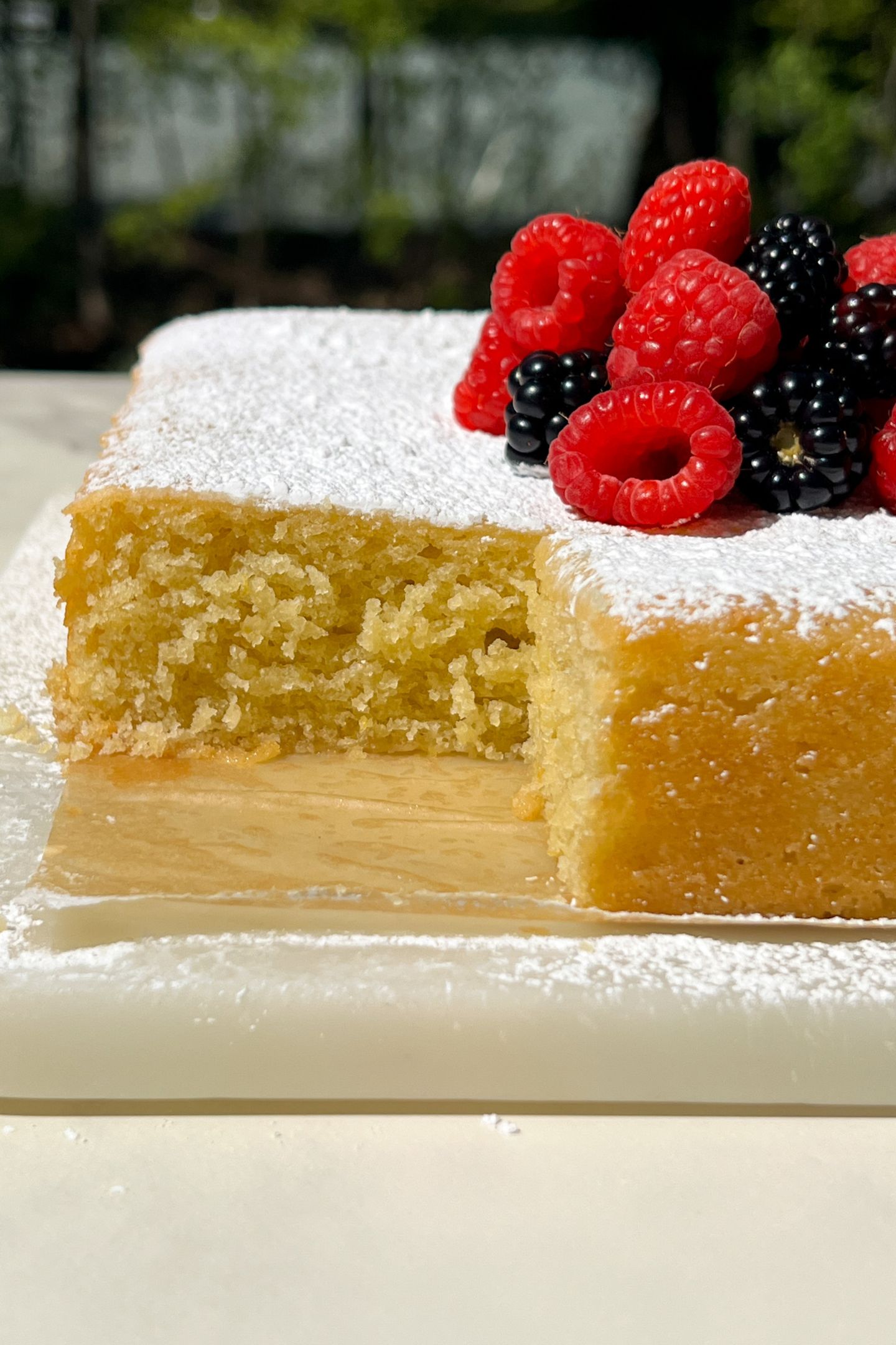 Lemon Olive Oil Cake topped with powdered sugar and berries with a slice taken out of it.