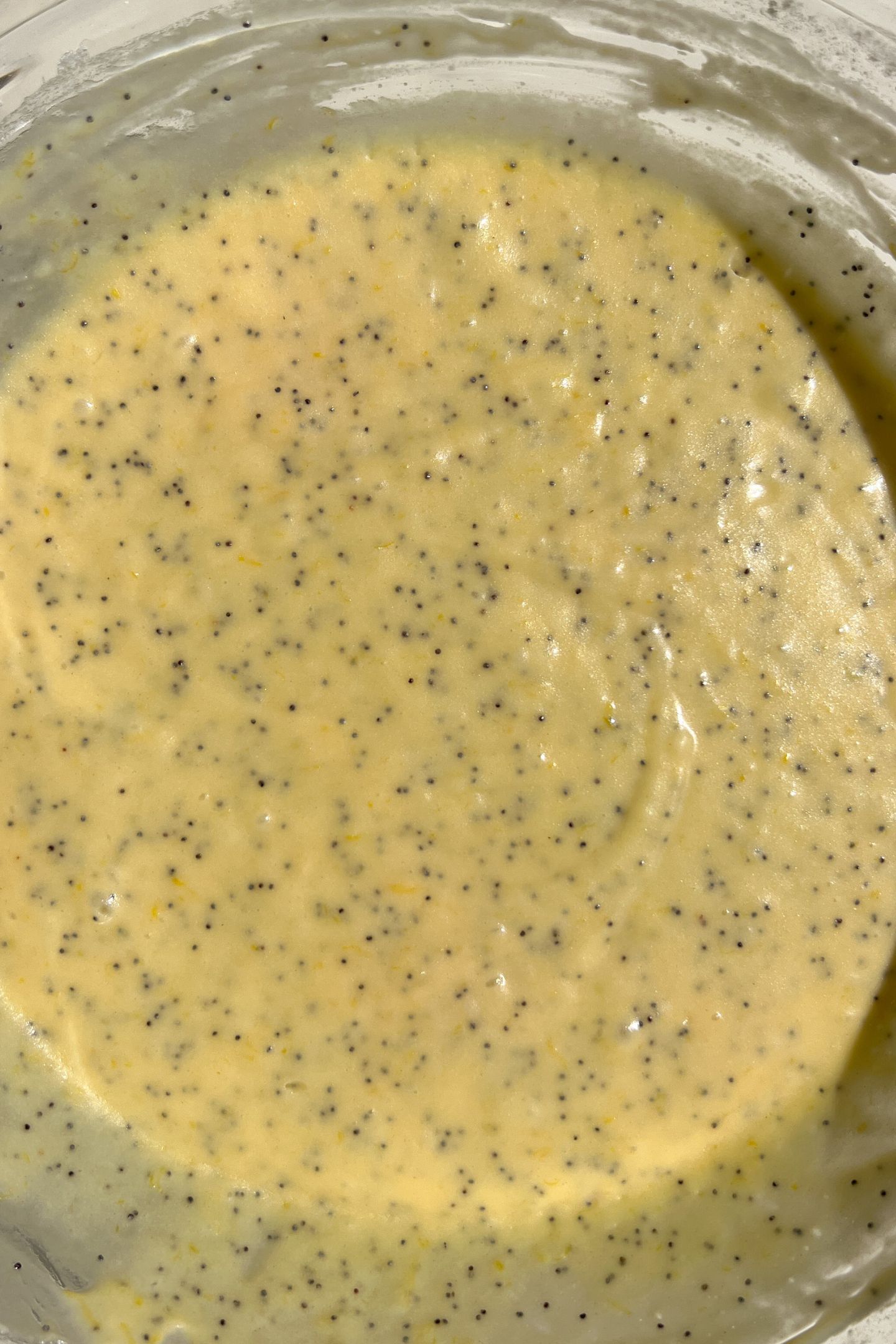 Wet and dry ingredients for the cupcake batter in a bowl with poppy seeds mixed together.